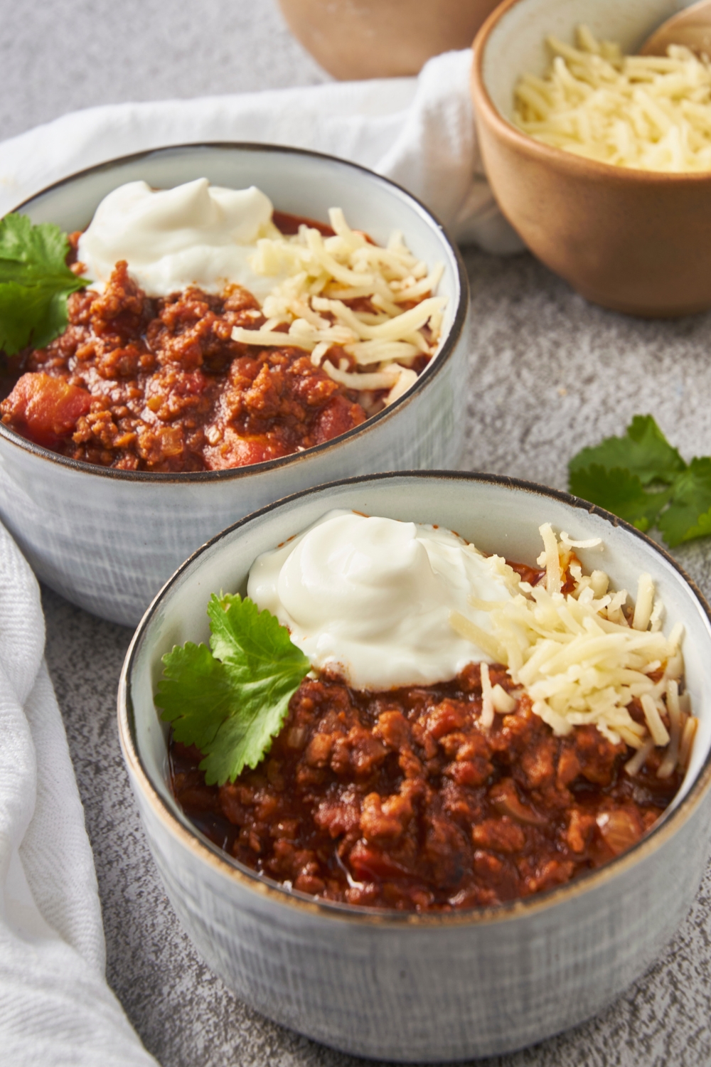 Two bowls of texas chili topped with shredded cheese and a dollop of sour cream.