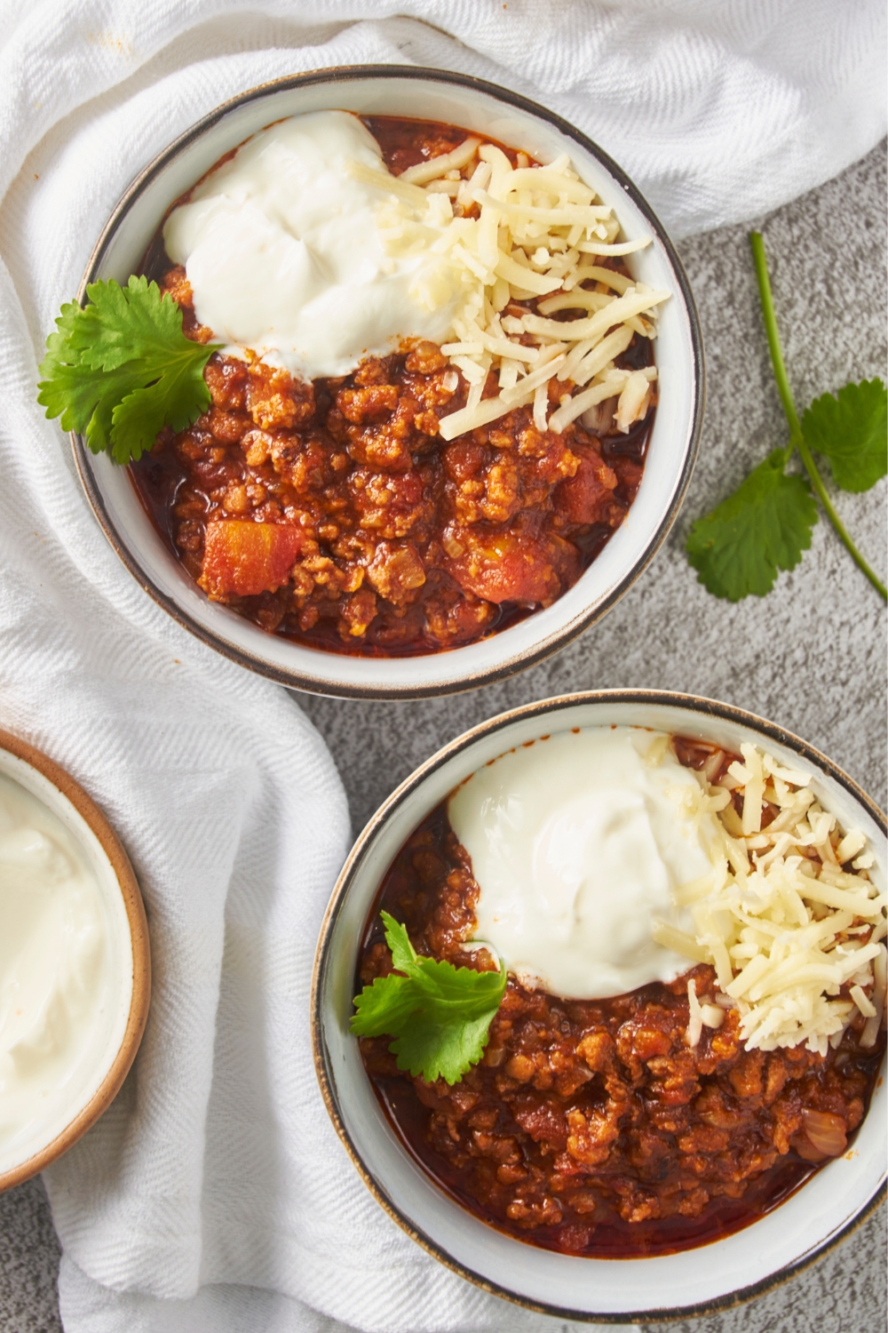 Two bowls of texas chili topped with shredded cheese and a dollop of sour cream.