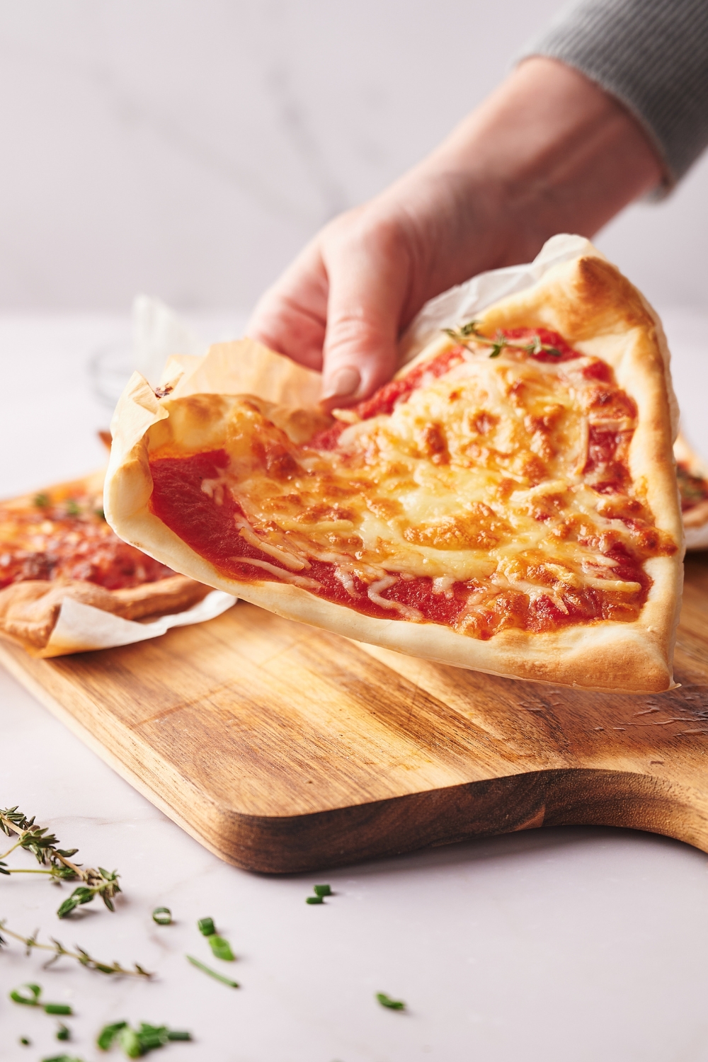A hand holding a slice of air fryer pizza.
