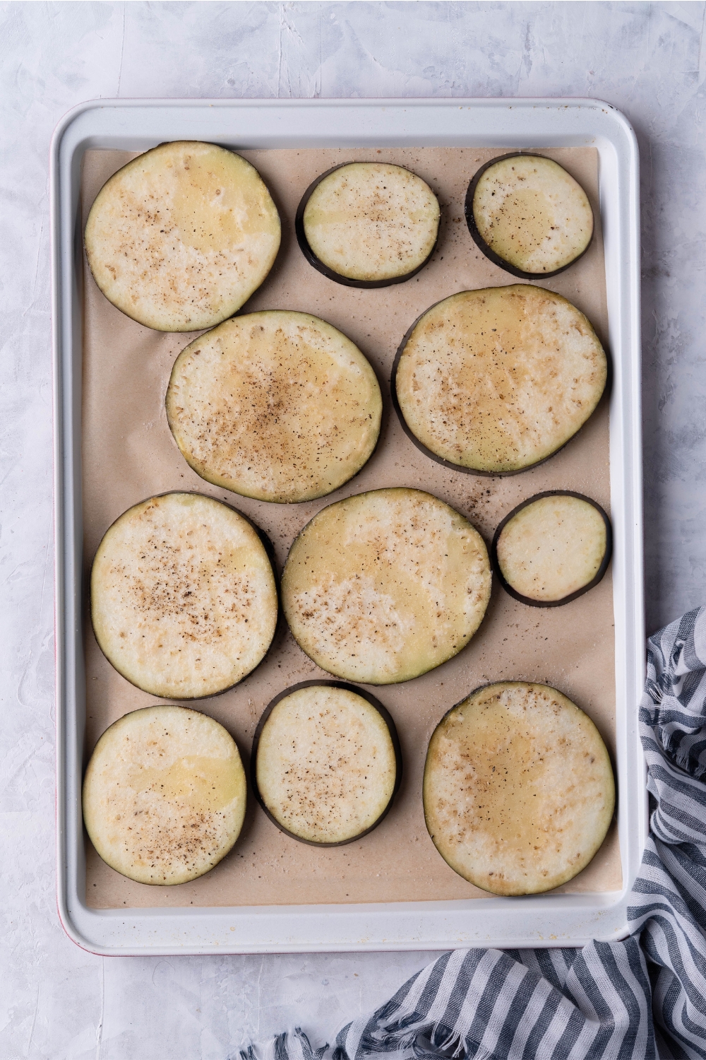 Ten seasoned eggplant slices on a sheet of parchment paper on a baking tray.