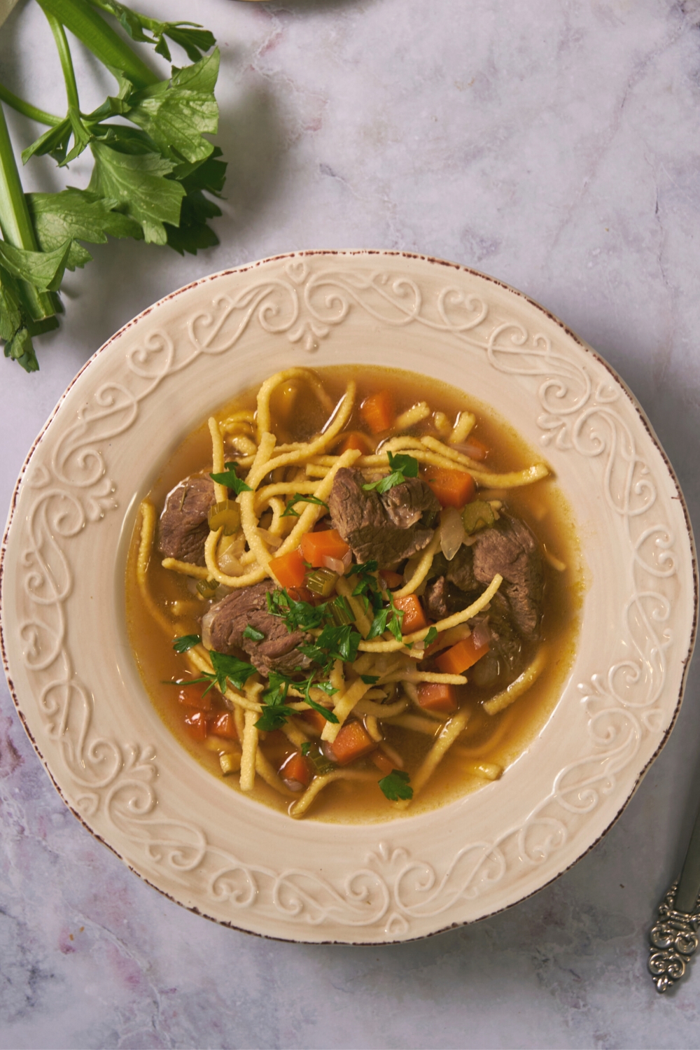 Beef cubes on top of noodles and chopped carrots in a bowl of broth.