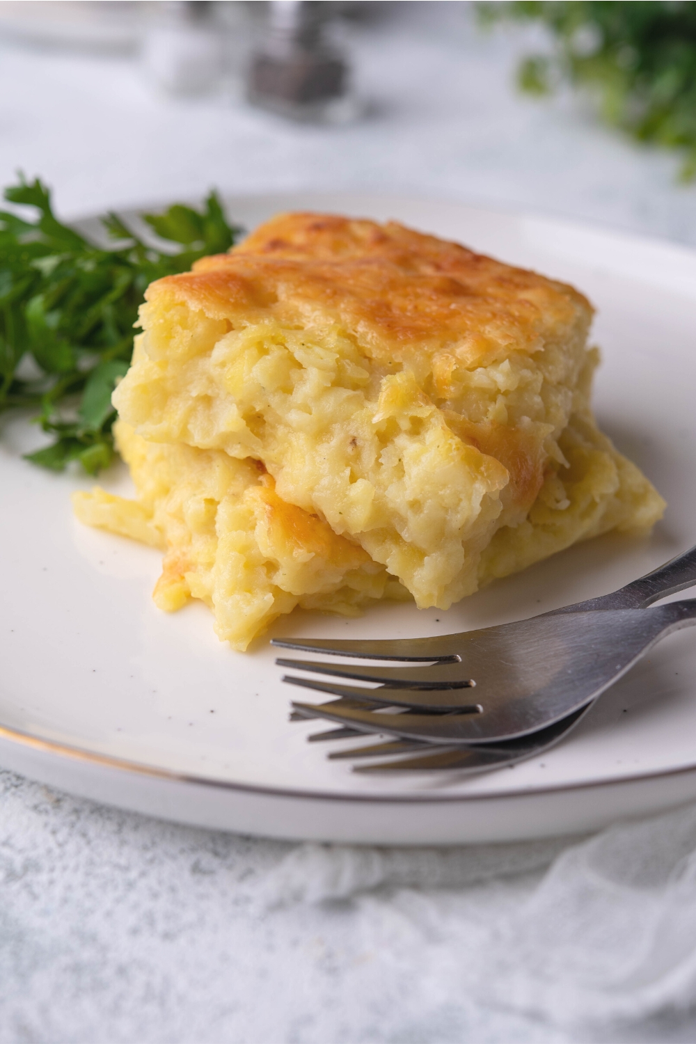 A square of cheesy potato casserole on top of another square on a plate.