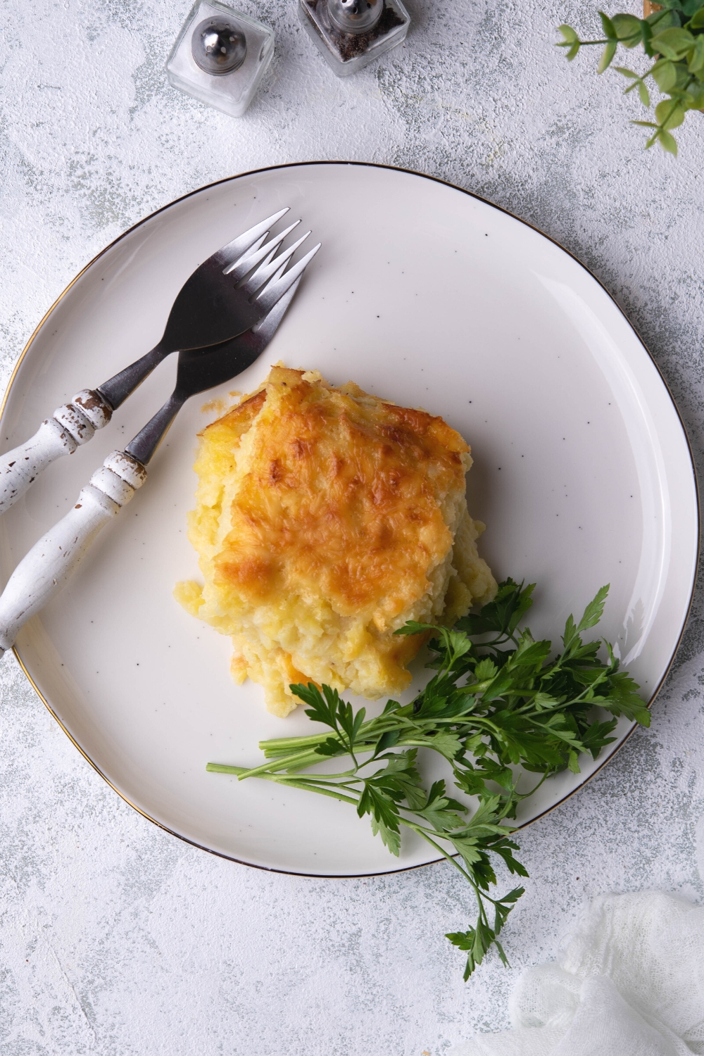 Two piece of cheesy potato casserole on top of one another on a white plate on a grey counter.