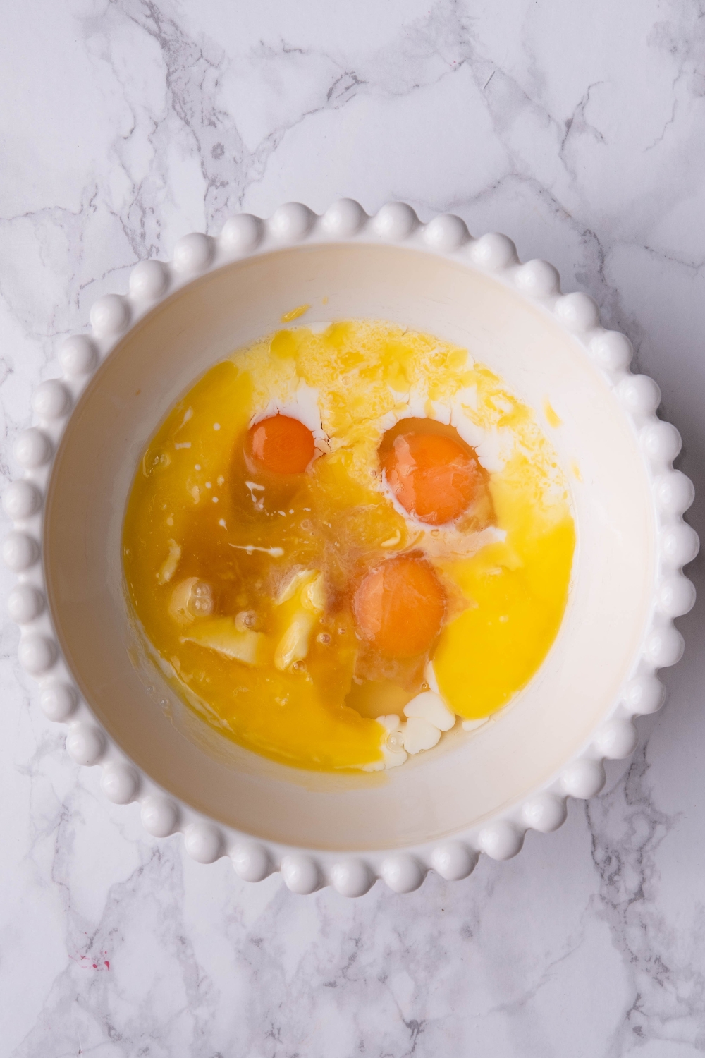 Three eggs, butter, and milk in a bowl.