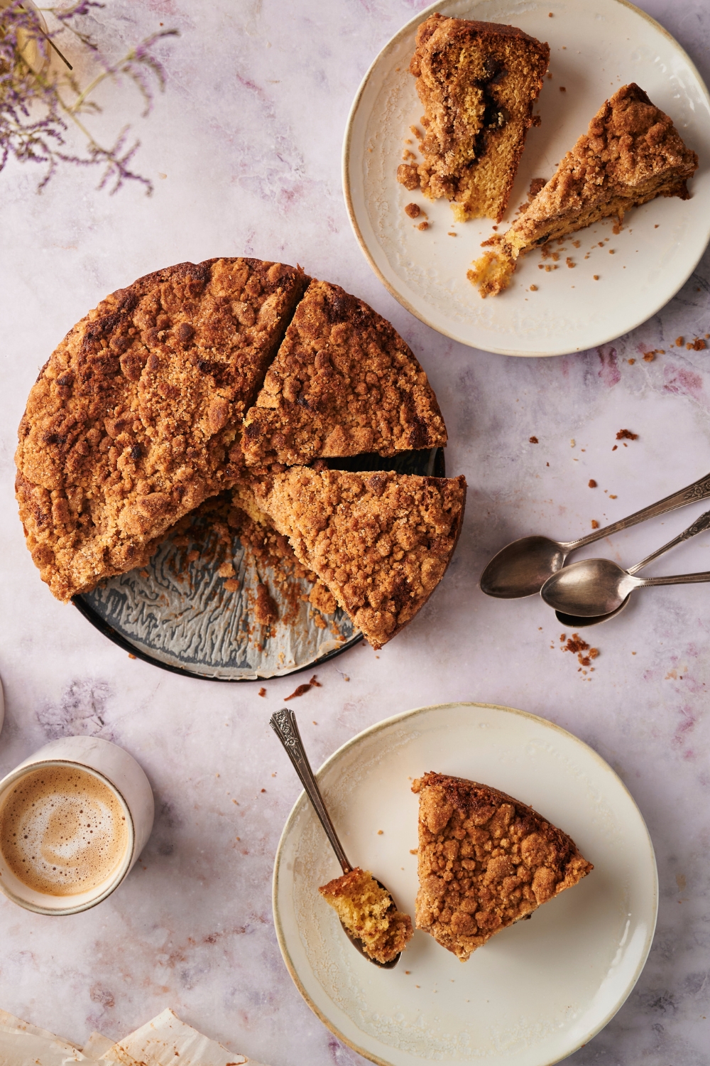 An overhead view of coffee cake on a pan with a slice taken out of it. A plate is sitting next to the pan with a slice of coffee cake on it with a spoonful of coffee cake next to it.