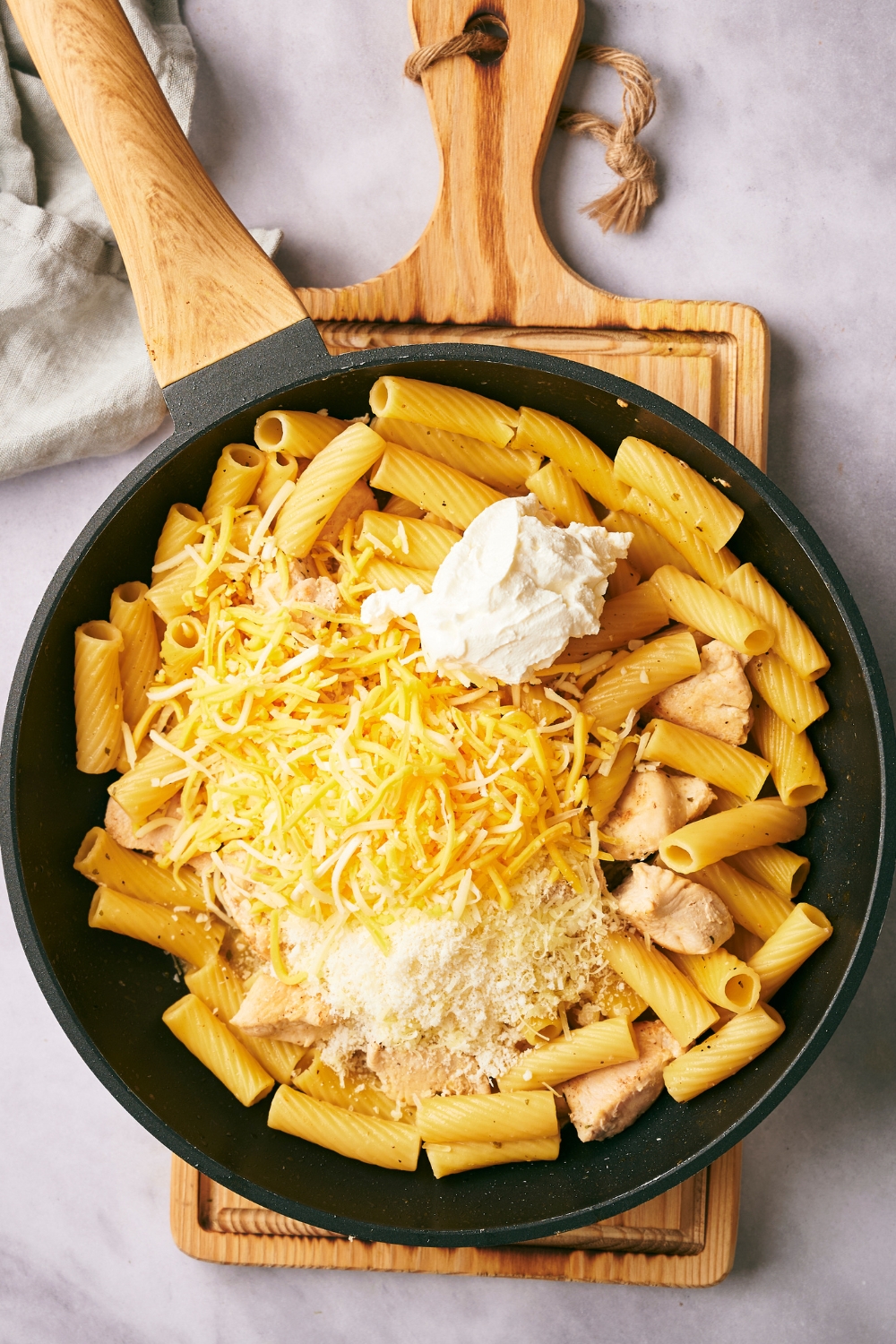 A large skillet with cooked noodles, cooked chicken, shredded cheese, Parmesan cheese, and cream cheese.