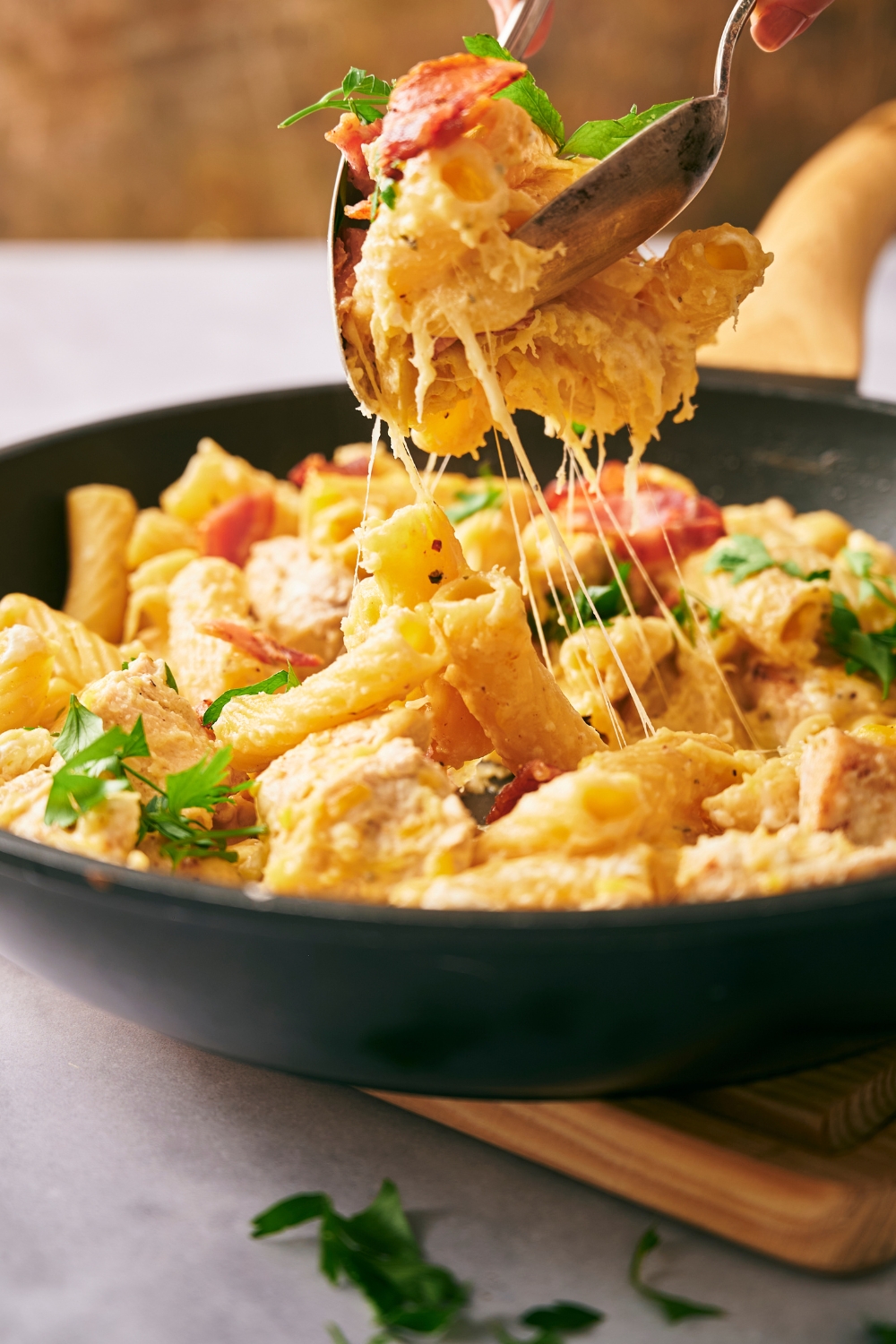 A large skillet with crack chicken pasta garnished with parsley. Two spoons are serving a large scoop.