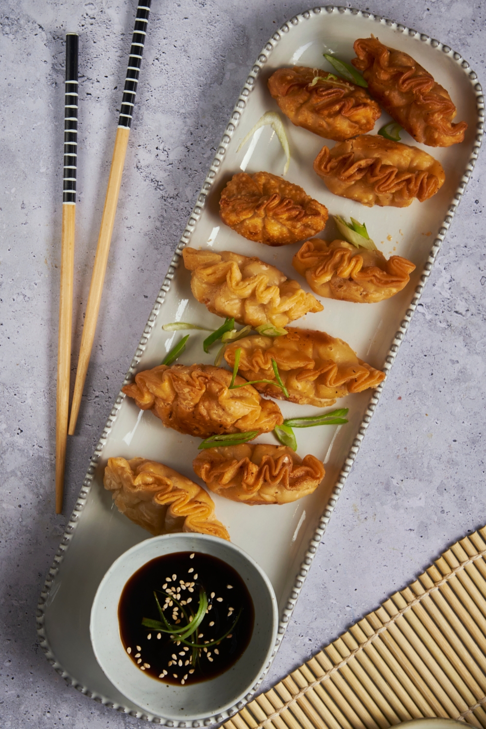 A serving plate with fried crab rangoon and a soy dipping sauce. Chop sticks are sitting next to the plate.