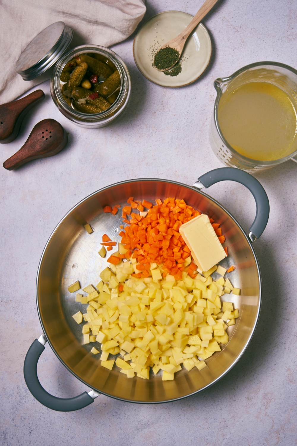 Diced potatoes, diced carrots, and a cube of butter in a pot.