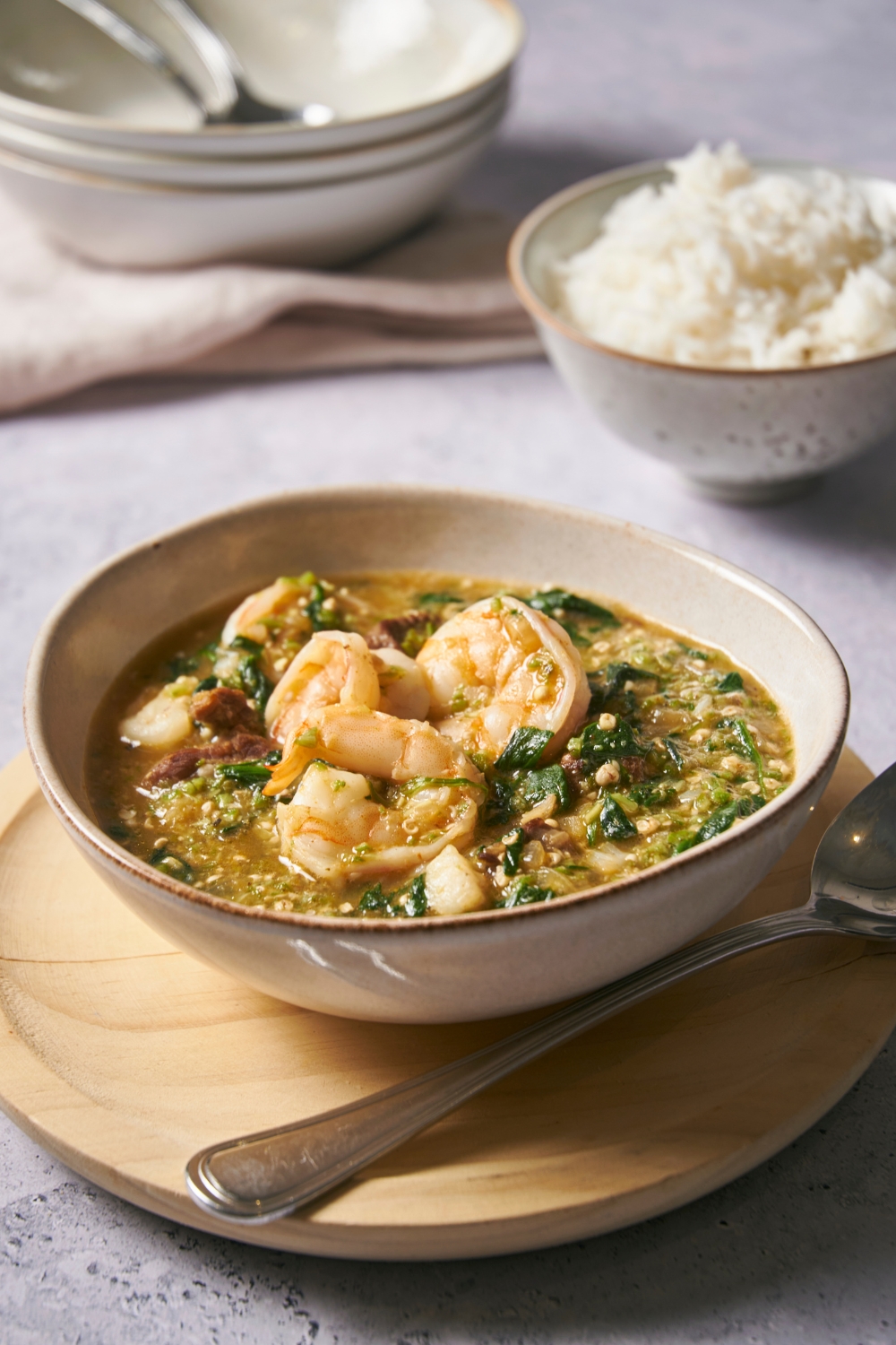 Three pieces of shrimp on top of okra soup in a bowl. Behind it is part of a bowl of white rice.