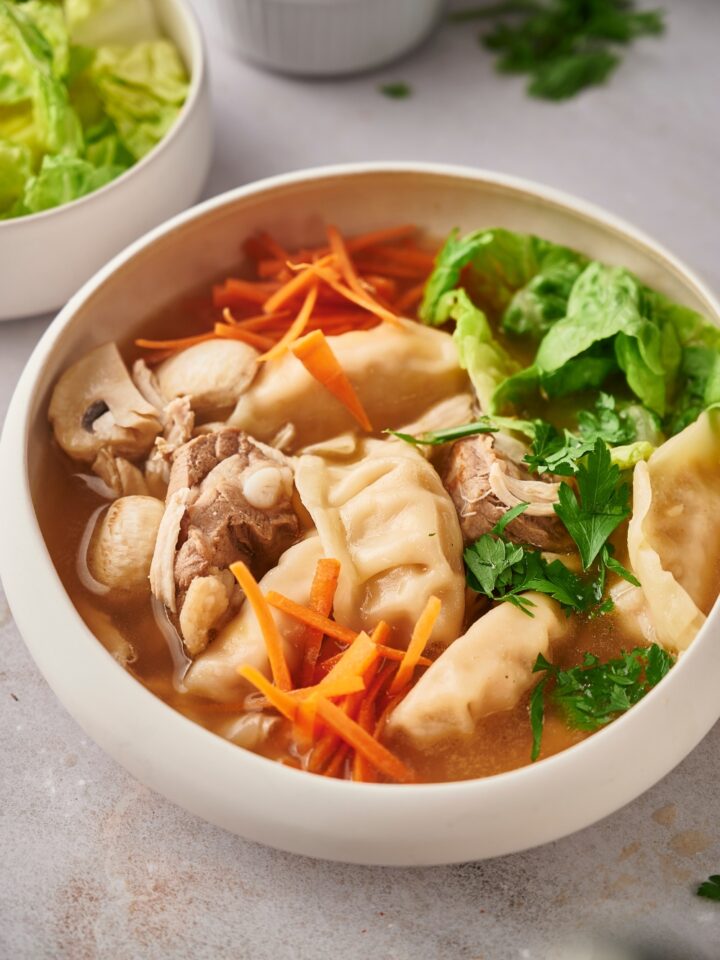 Lettuce, shredded carrots, wontons, chicken, and pork in broth that is in a white bowl.