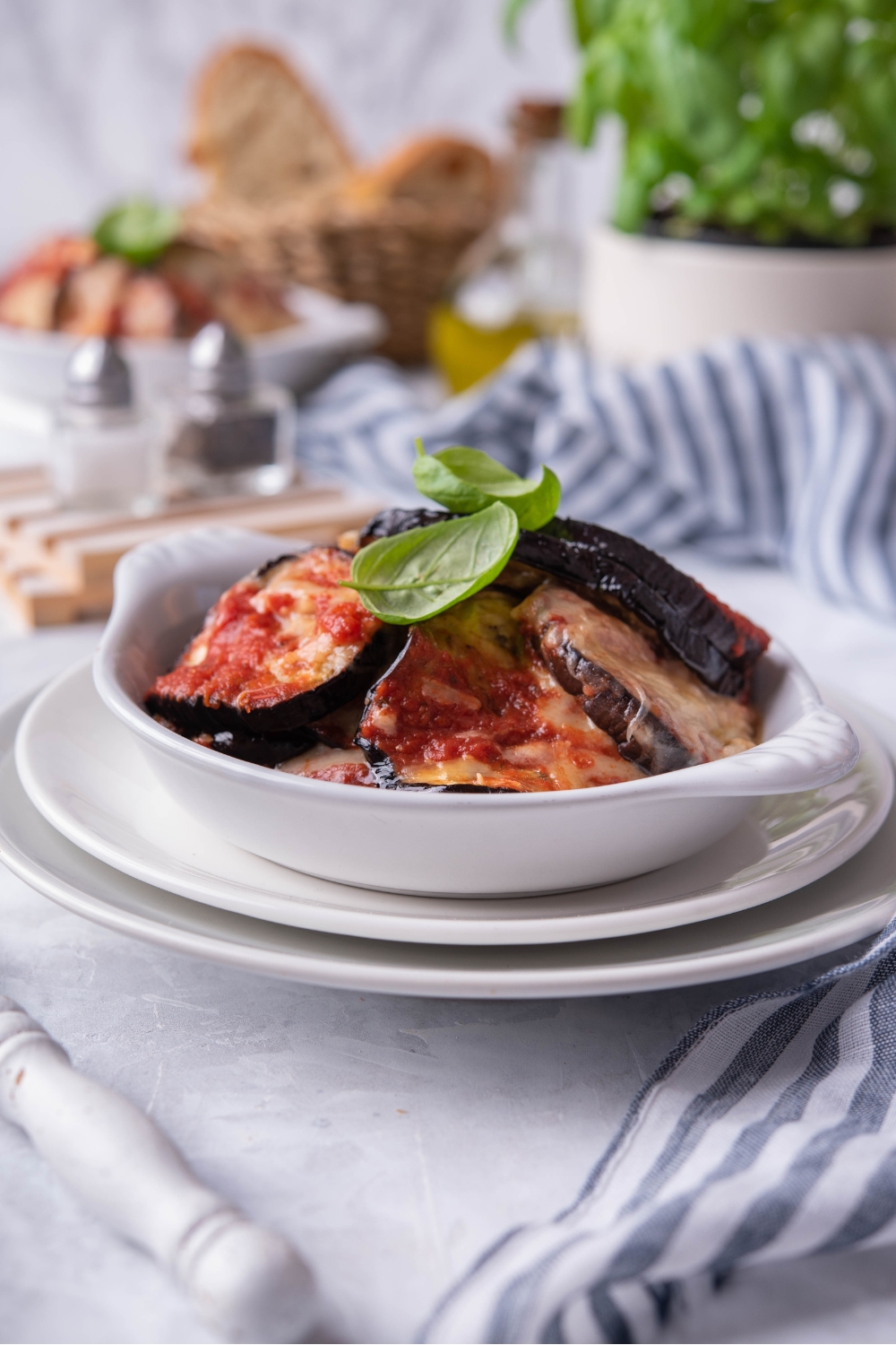 A white bowl filled with sliced eggplant with red sauce and melted cheese on top of them.