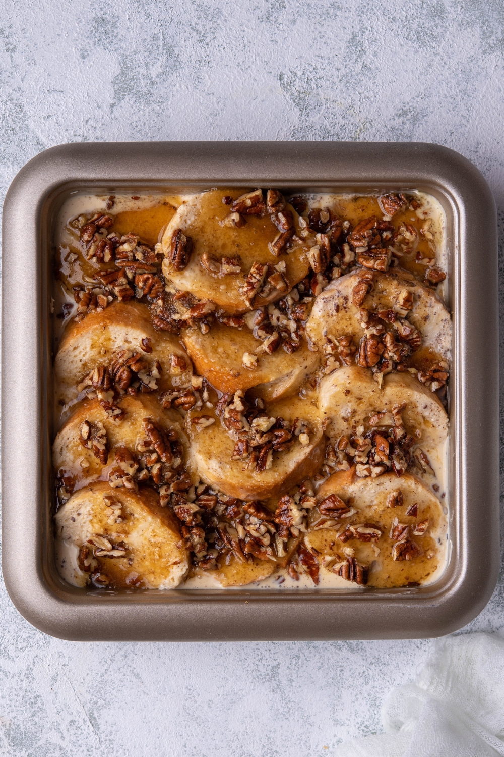 A pan with uncooked french toast casserole topped with pecans.