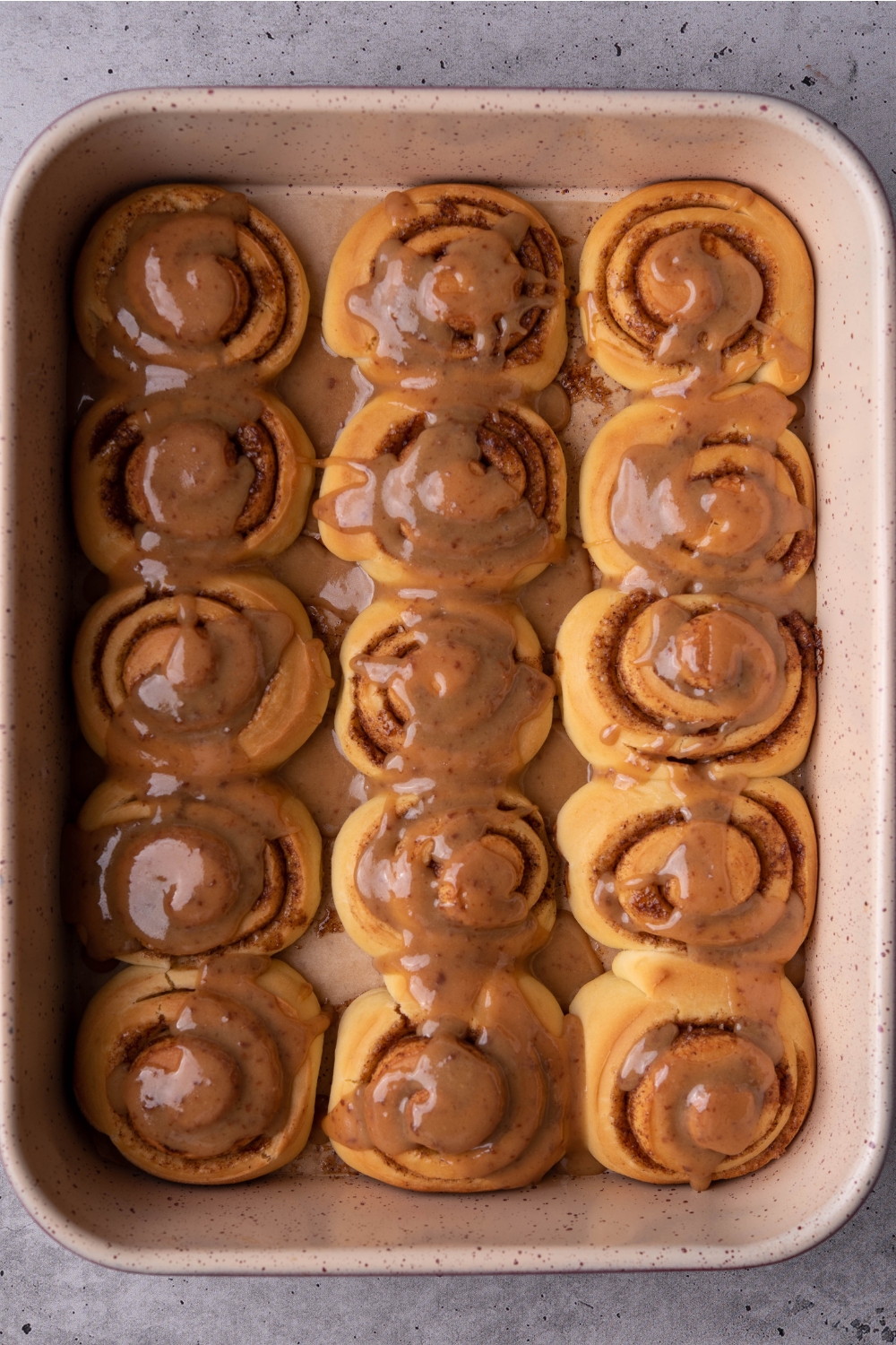 A baking pan with baked cinnamon rolls topped with caramel sauce.