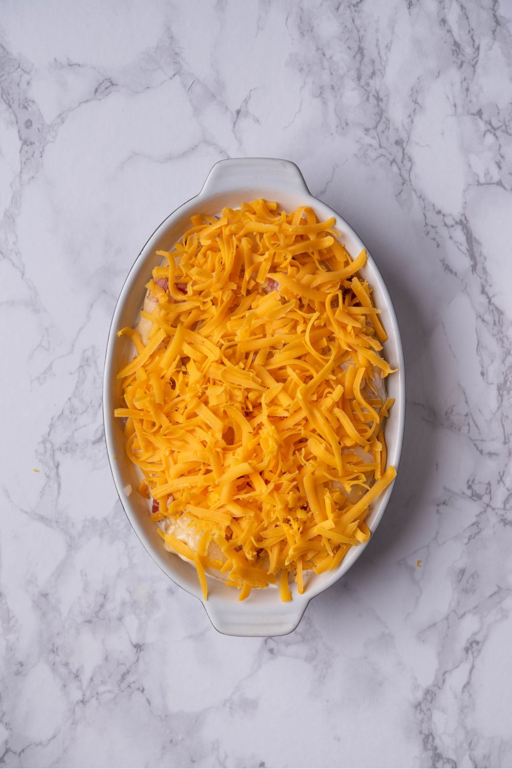 A bunch of shredded cheddar cheese on top of pierogis and a creamy sauce in a casserole dish.
