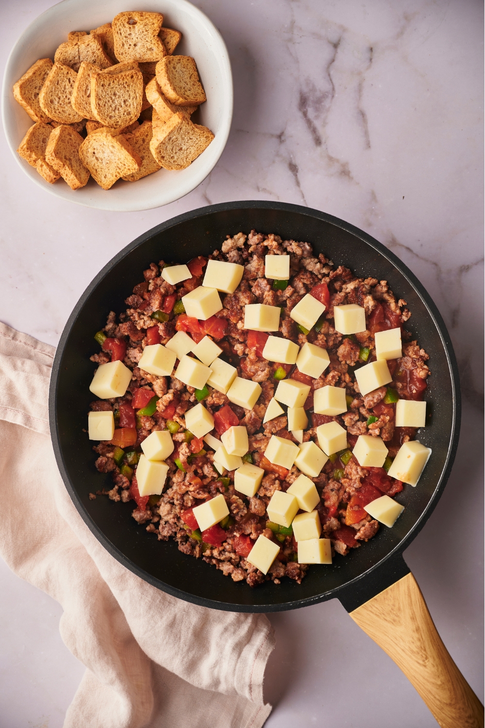 Cubed cheese on top of rotel tomatoes on ground sausage in a skillet.