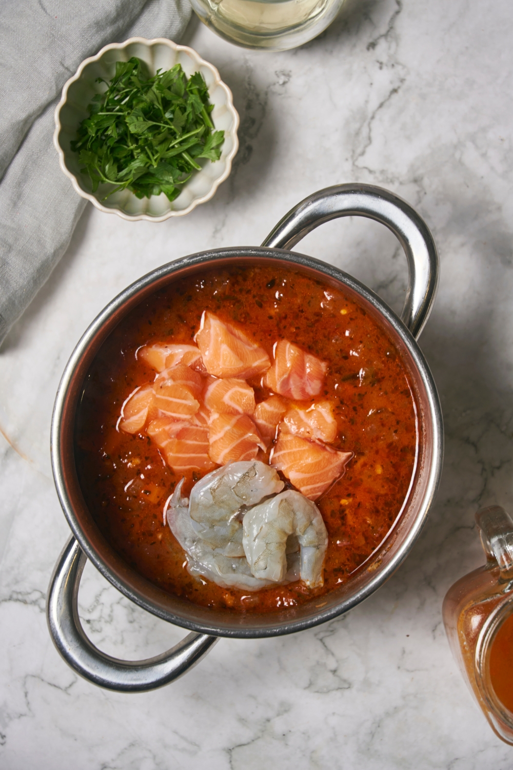 Cubed salmon and shrimp on top of tomato broth in a pot.