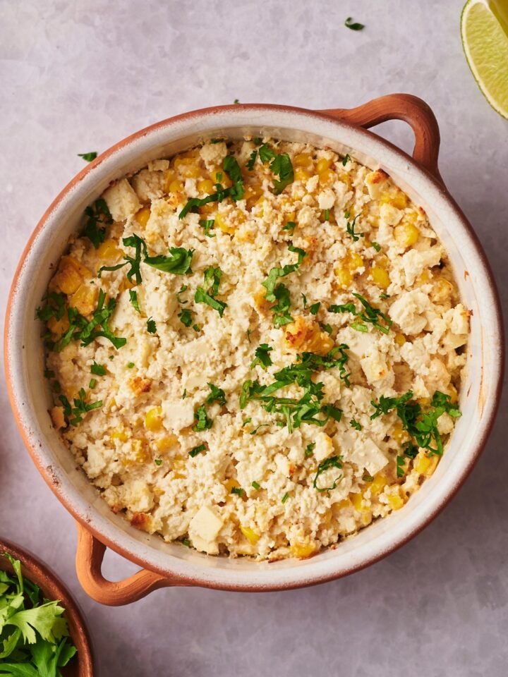 A casserole dish with Mexican corn casserole garnished with cilantro.