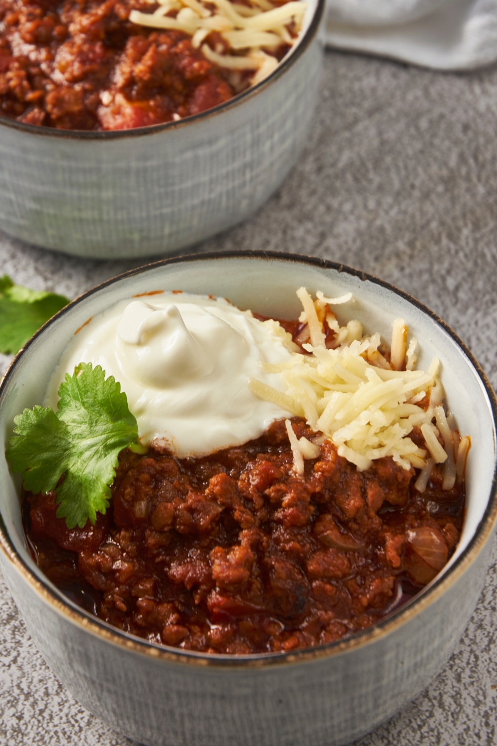 A bowl of texas chili topped with shredded cheese and a dollop of sour cream.