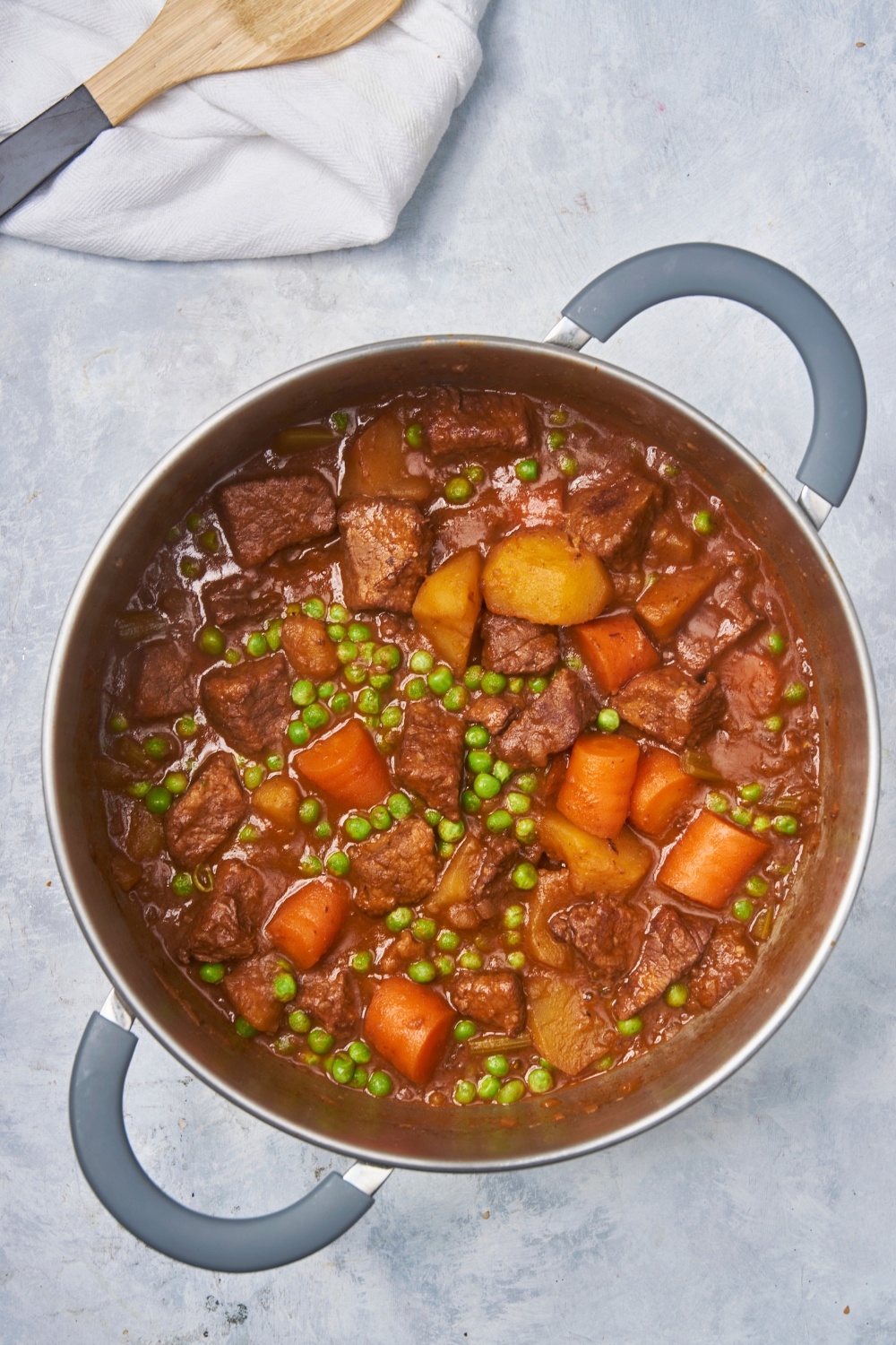 Peas, potatoes, carrots, and stew meat in broth in a pot.
