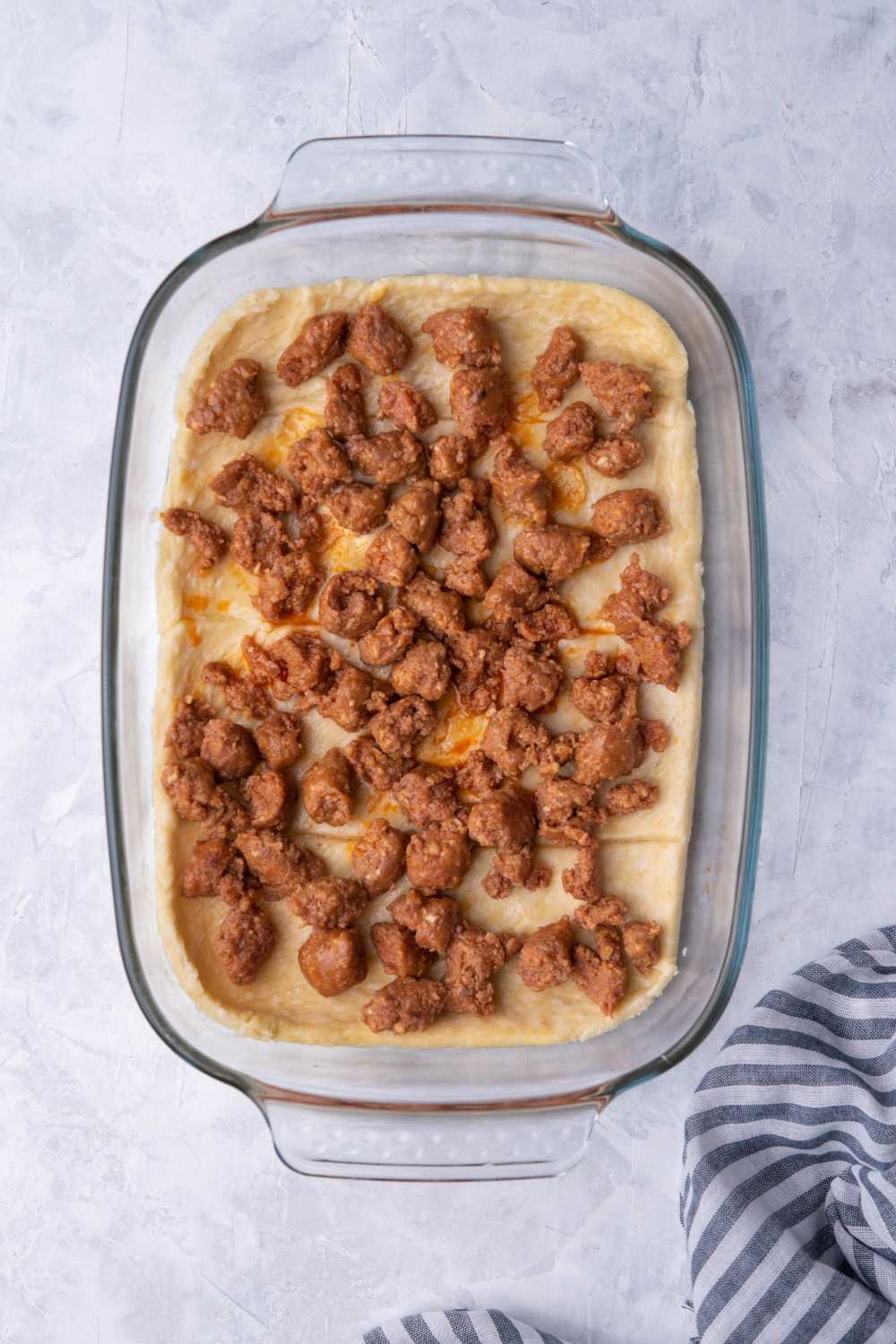 A casserole dish filled with crescent roll dough and pieces of uncooked sausage.