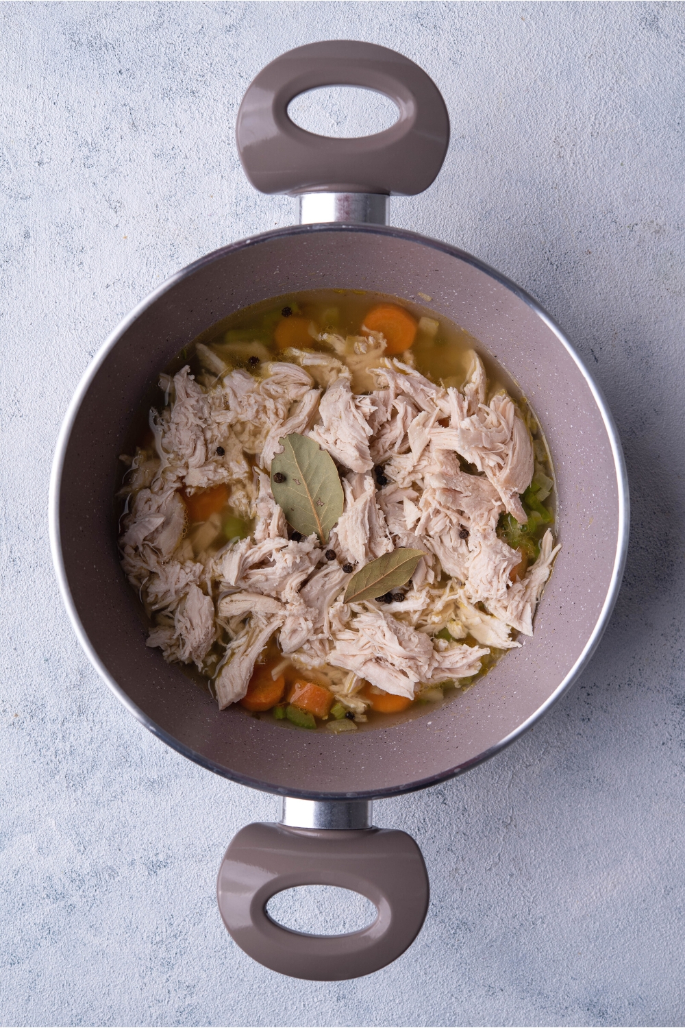 Shredded chicken on top of veggies and broth in a pot.