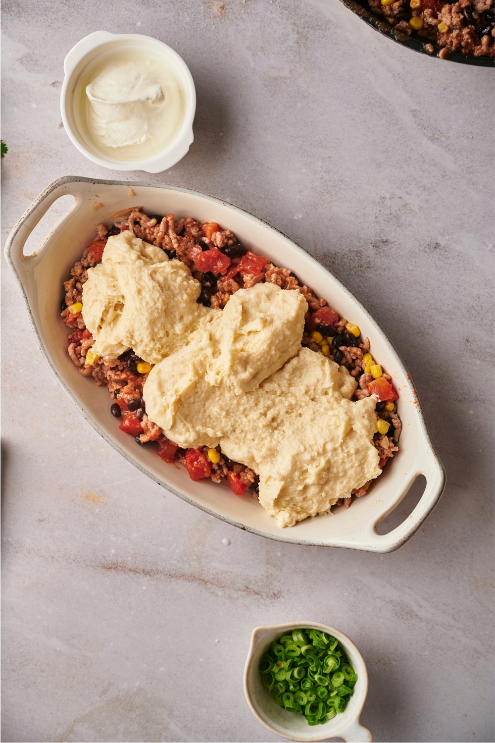 Cornbread batter on top of a ground beef mixture in a casserole dish.