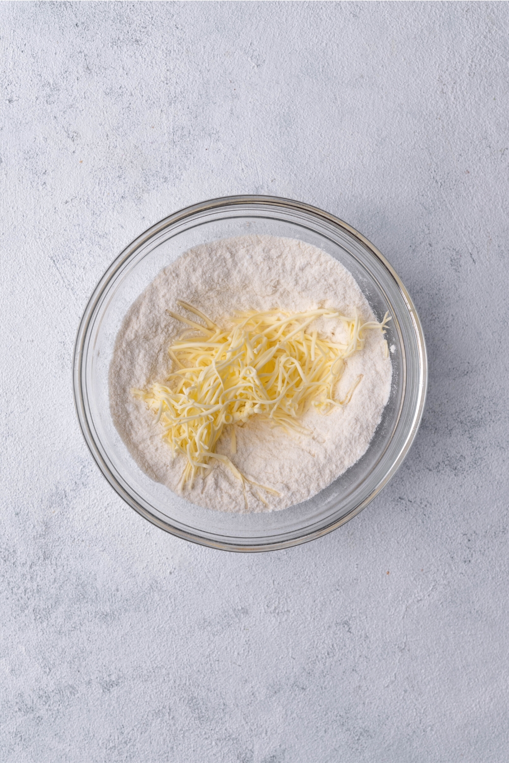 Grated butter on top of flour in a glass bowl.