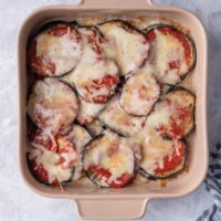 Melted mozzarella cheese on top of sauce on eggplant slices in a square baking dish.