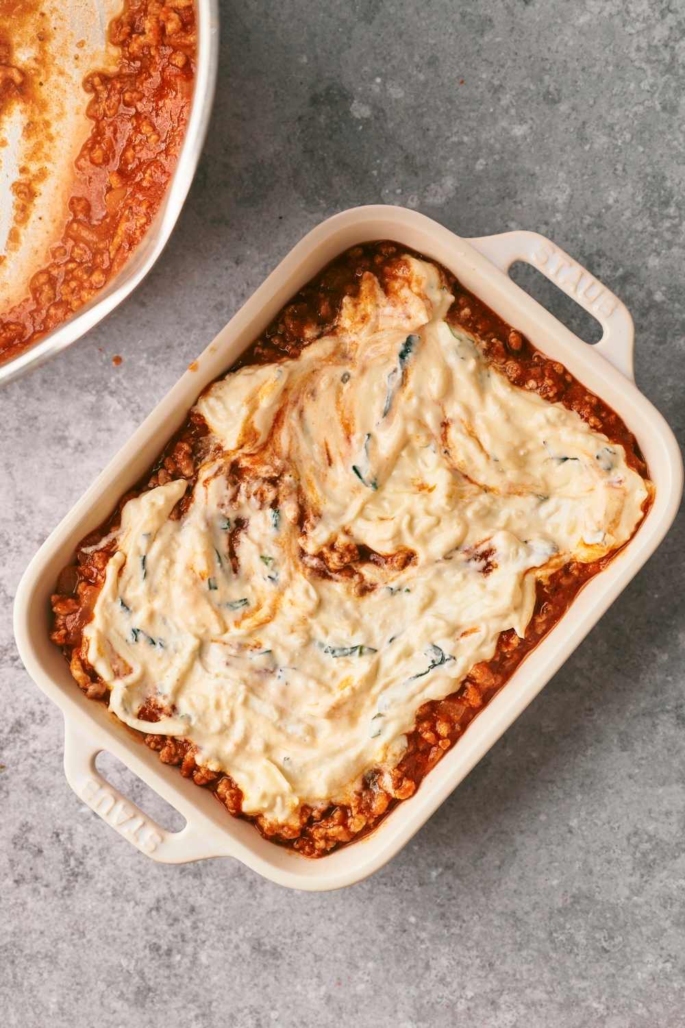 Ricotta cheese spread on top of beef pasta sauce in a casserole dish.