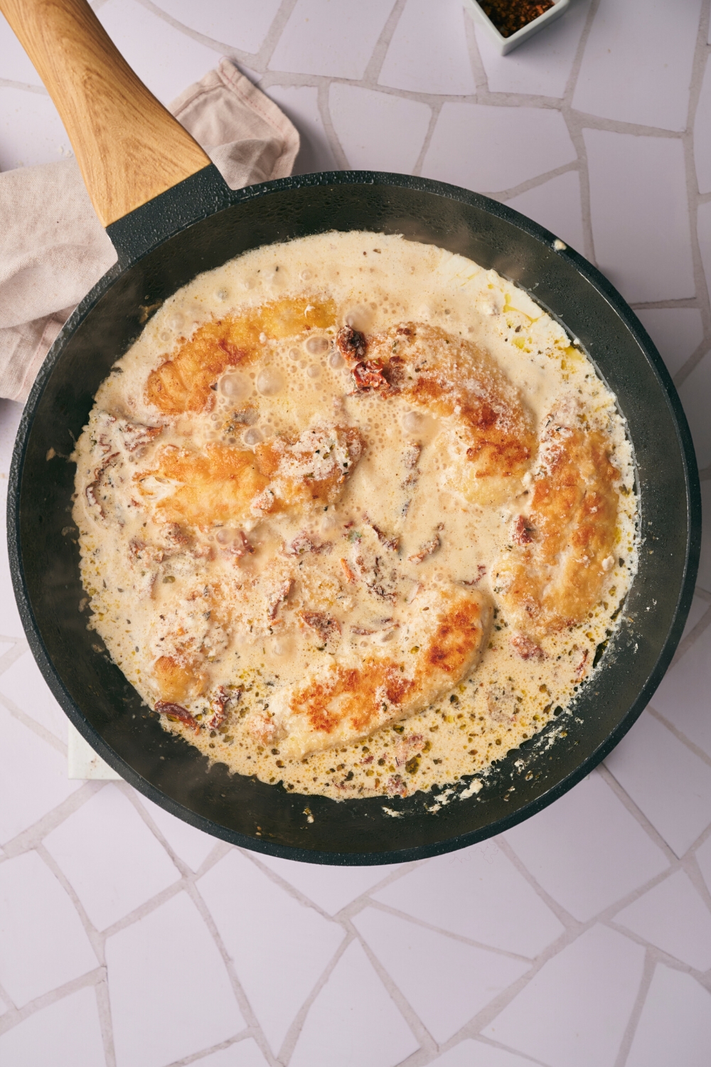 A few pieces of chicken cooking in a cream sauce in a skillet.