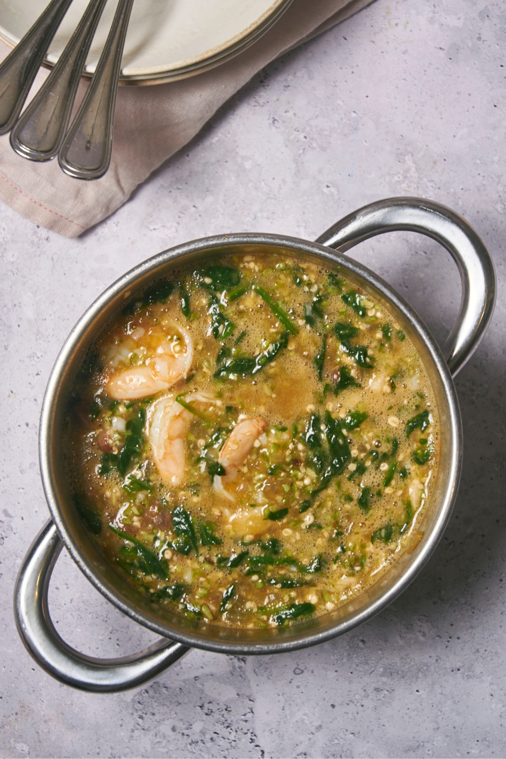 Shrimp, spinach, and ground okra in a pot of soup broth.