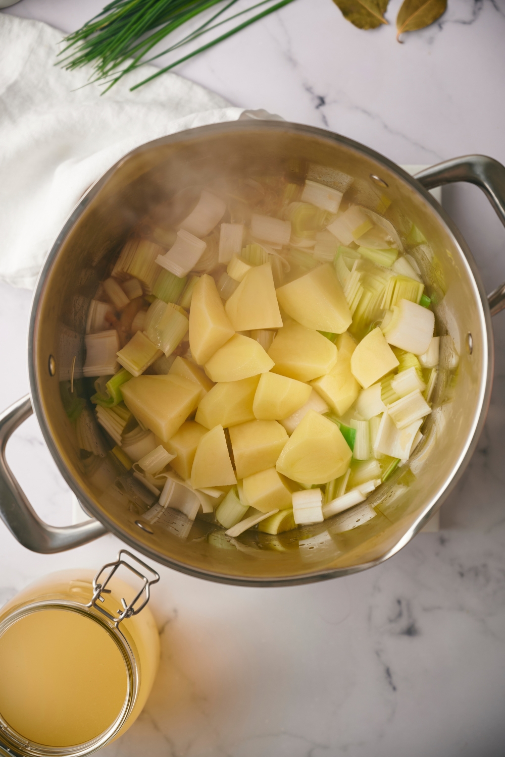 Diced potatoes on top of chopped leeks cooking a pot.