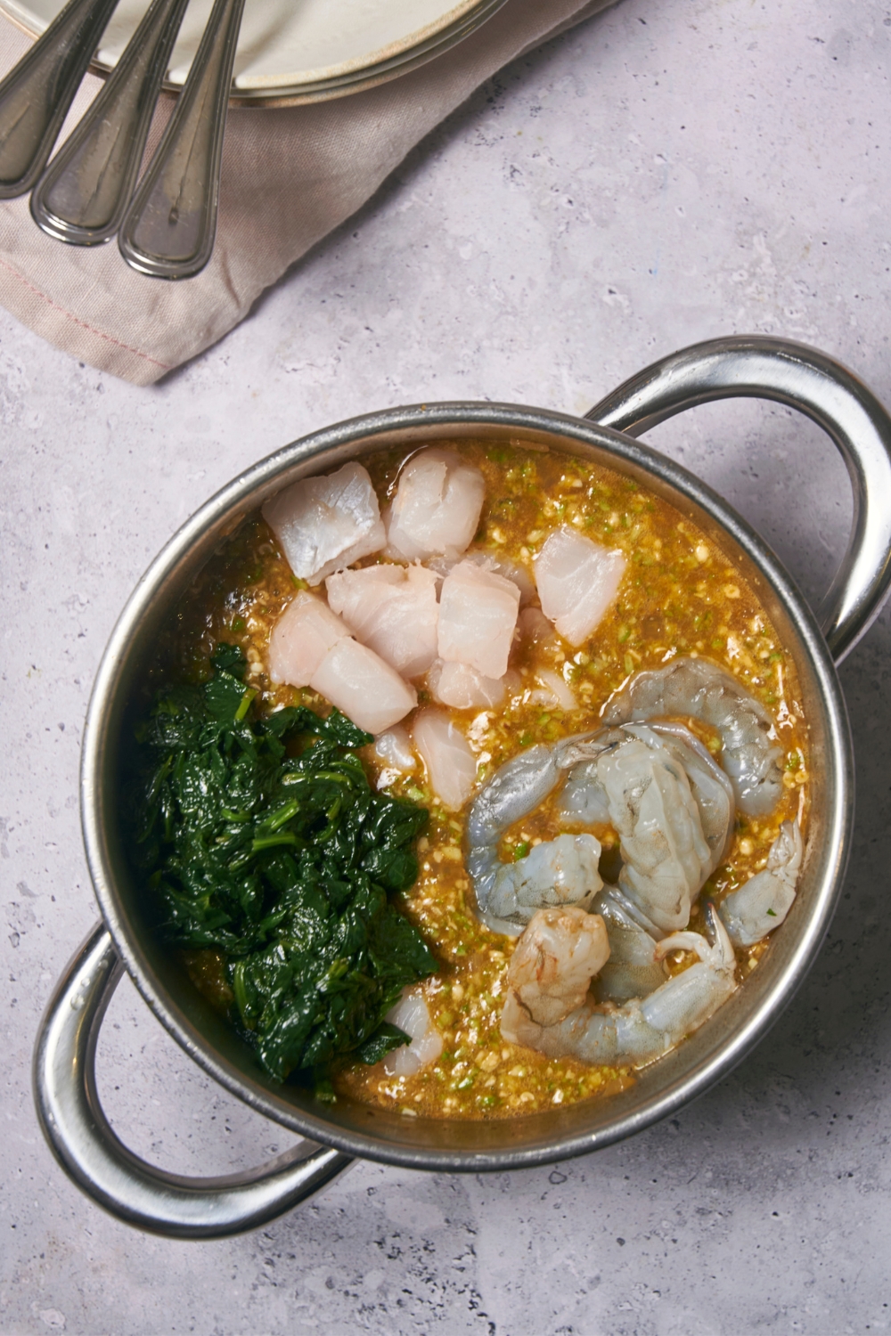 White fish, spinach, and shrimp on top of broth in a pot.