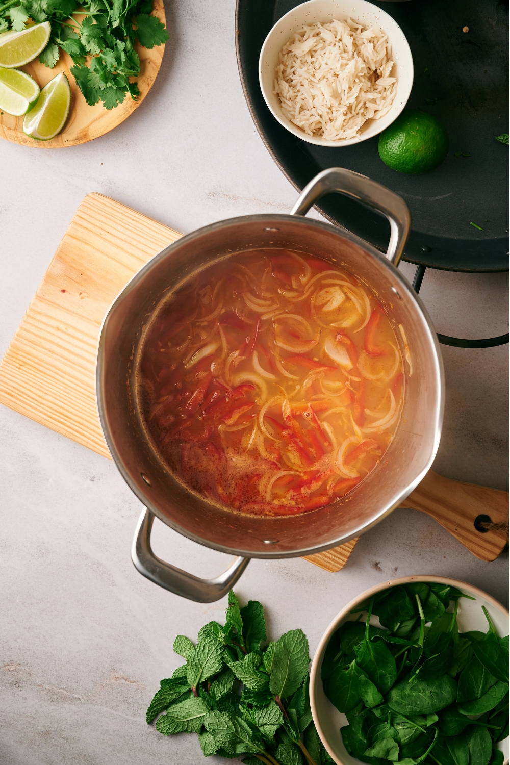Broth in a pot with sliced red bell peppers and onions.
