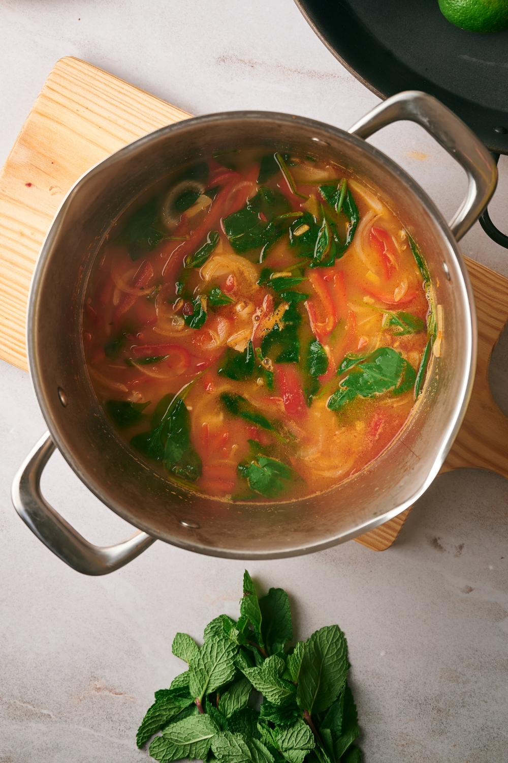 Wilted spinach, sliced red bell peppers, and onions in broth in a pot.