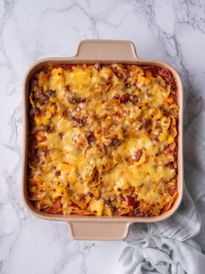 Melted shredded cheese on top of a sloppy joe casserole in a baking dish.