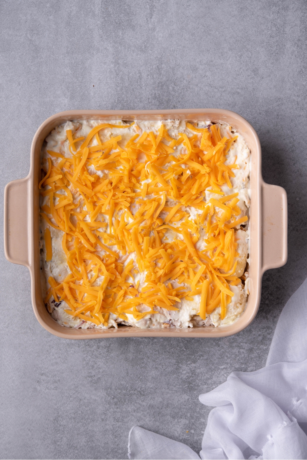 Cheese on top of the creamy mixture in a square casserole dish.