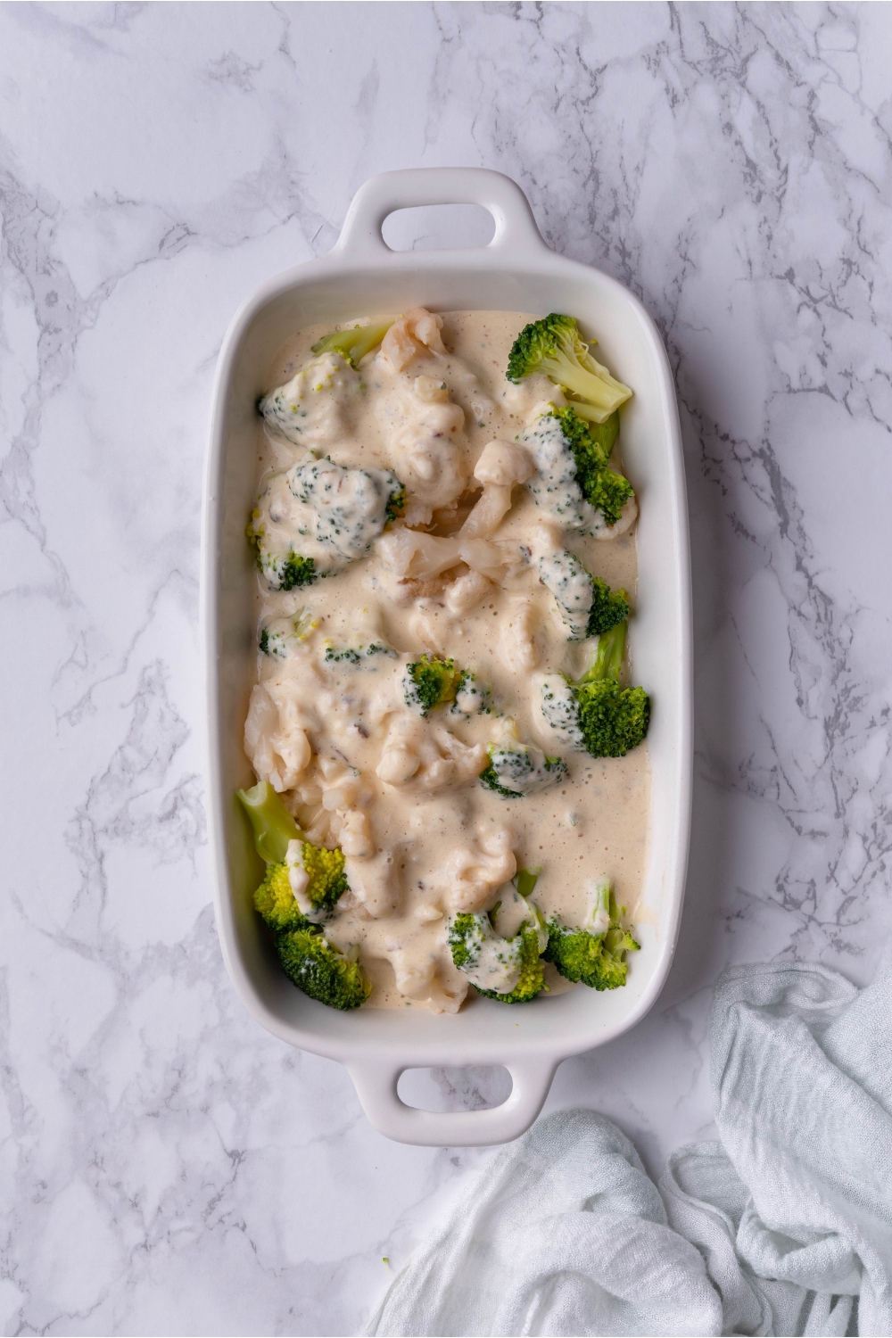 Creamy soup on top of broccoli and cauliflower in a casserole dish.