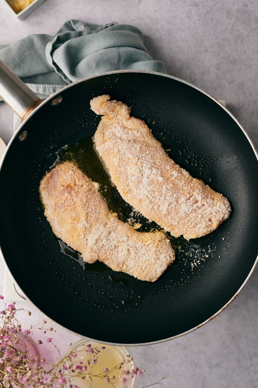 A frying pan with breaded chicken being cooked in hot oil.