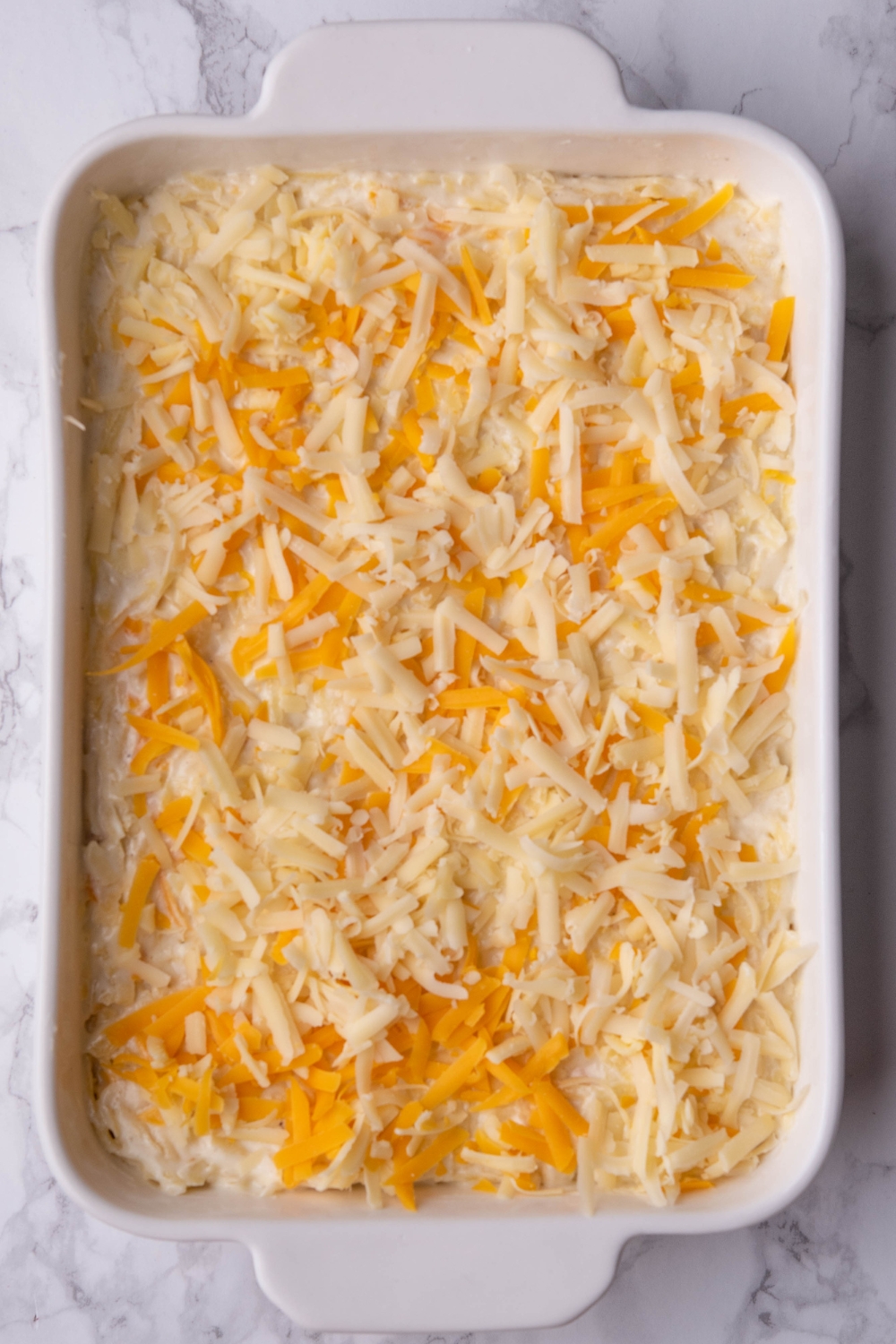 A casserole dish with uncooked hash brown casserole in it.