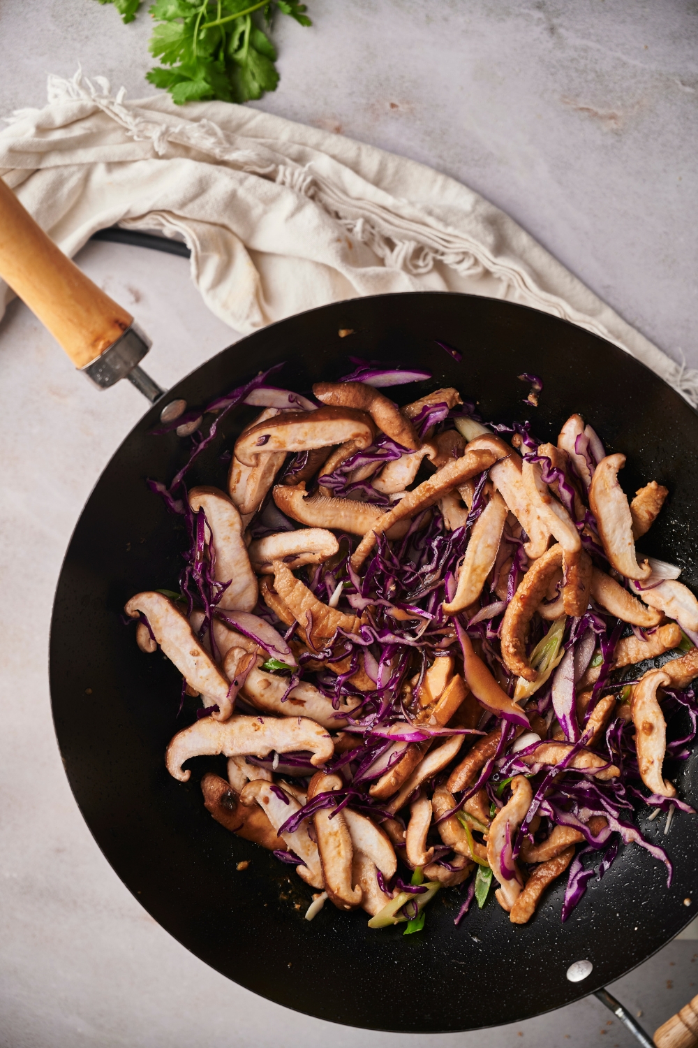 Part of a skillet with moo shu pork and shredded purple cabbage in a wok.