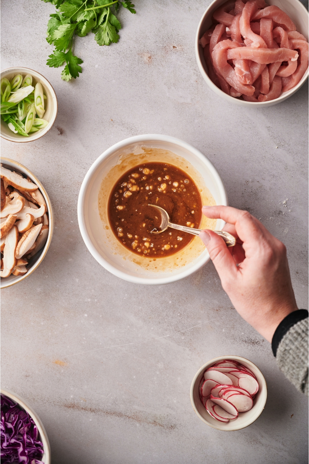 A hand holding a spoon in a bowl with moo shoo pork marinade.
