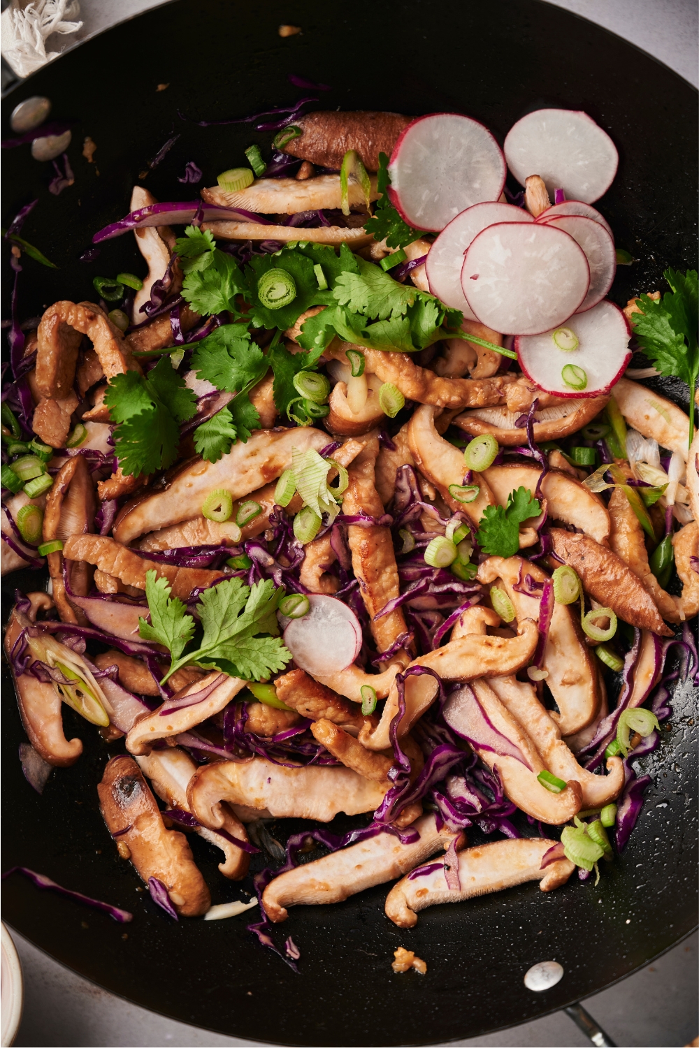 Sliced raddishes, green onion, purple cabbage, and moo shu pork in a wok.