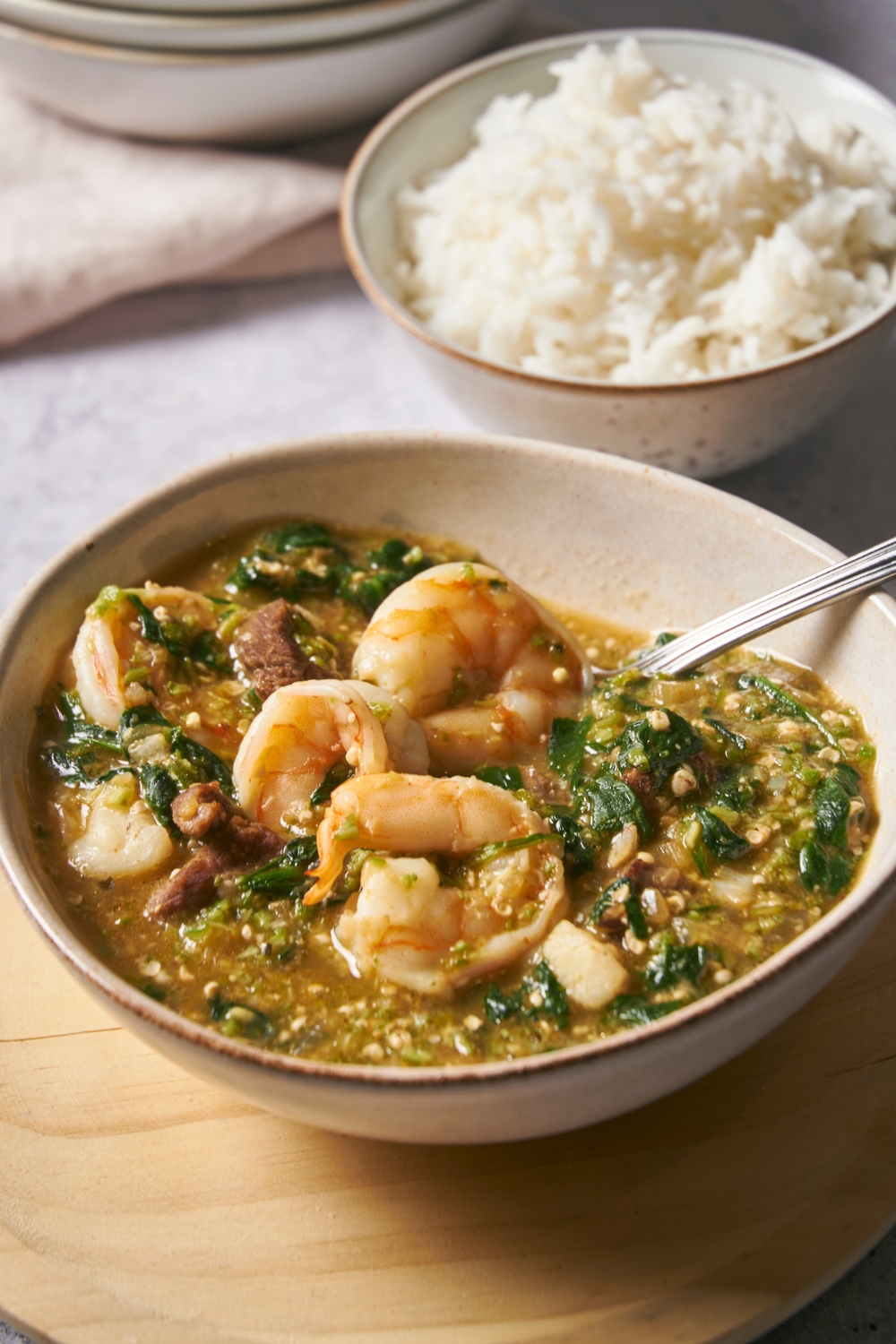 Shrimp, steak, spinach, and ground okra in a bowl of broth.