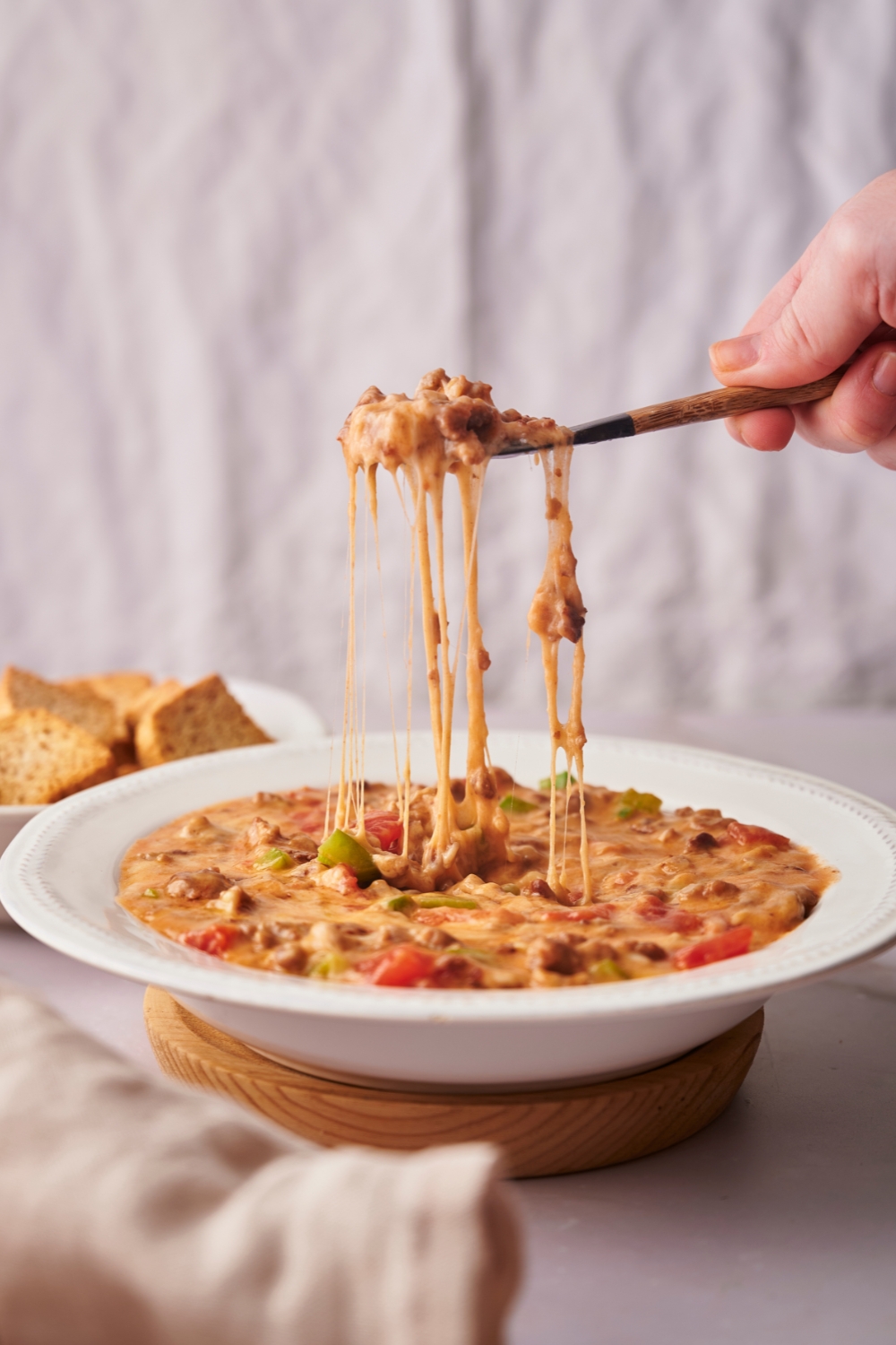 A hand holding a spoon that has Rotel dip on it being pulled from a bowl of rotel dip.