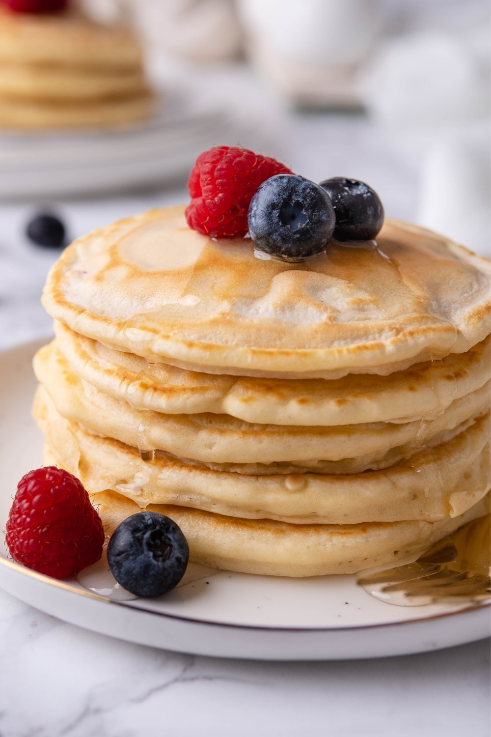 A stack of pancakes drizzled with maple syrup and topped with fresh berries on a plate.