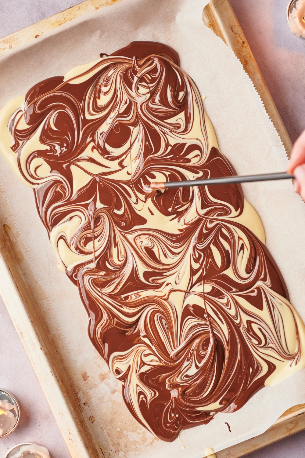 Melted chocolate in a checkered pattern on parchment paper. A straw is creating a marbled pattern.