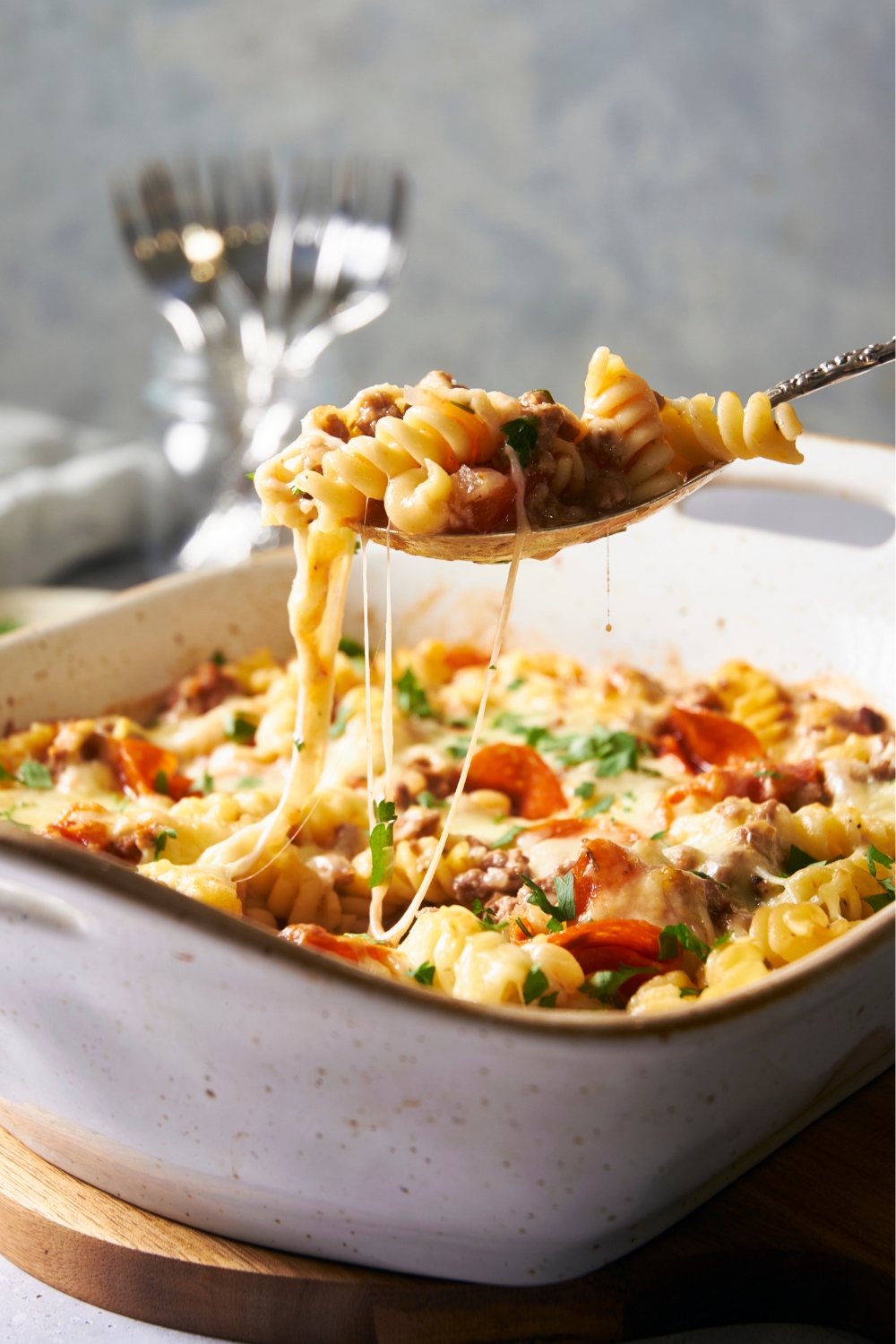 A deep baking dish with pizza pasta in it. A spoon has a scoop of the pasta pizza and is holding it over the dish.