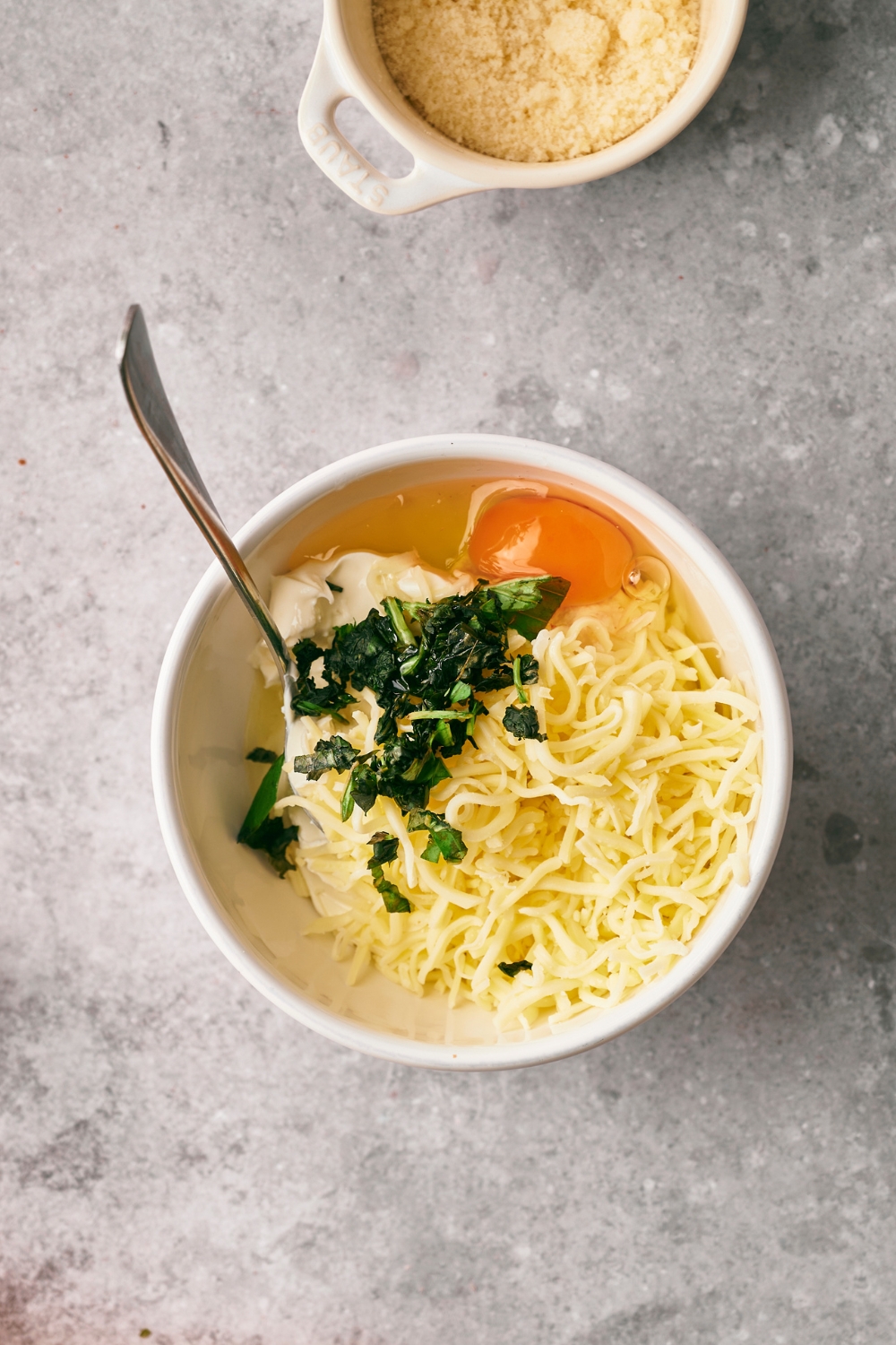 Shredded cheese, an egg, basil, and ricotta cheese in a bowl.